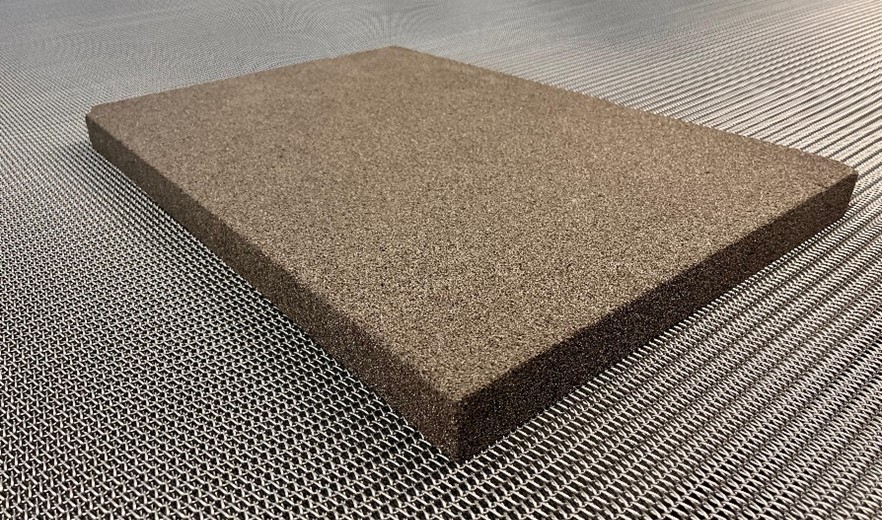 A rectangular brown composite board with a textured surface rests on a ribbed metal floor, conveying a modern and industrial feel.