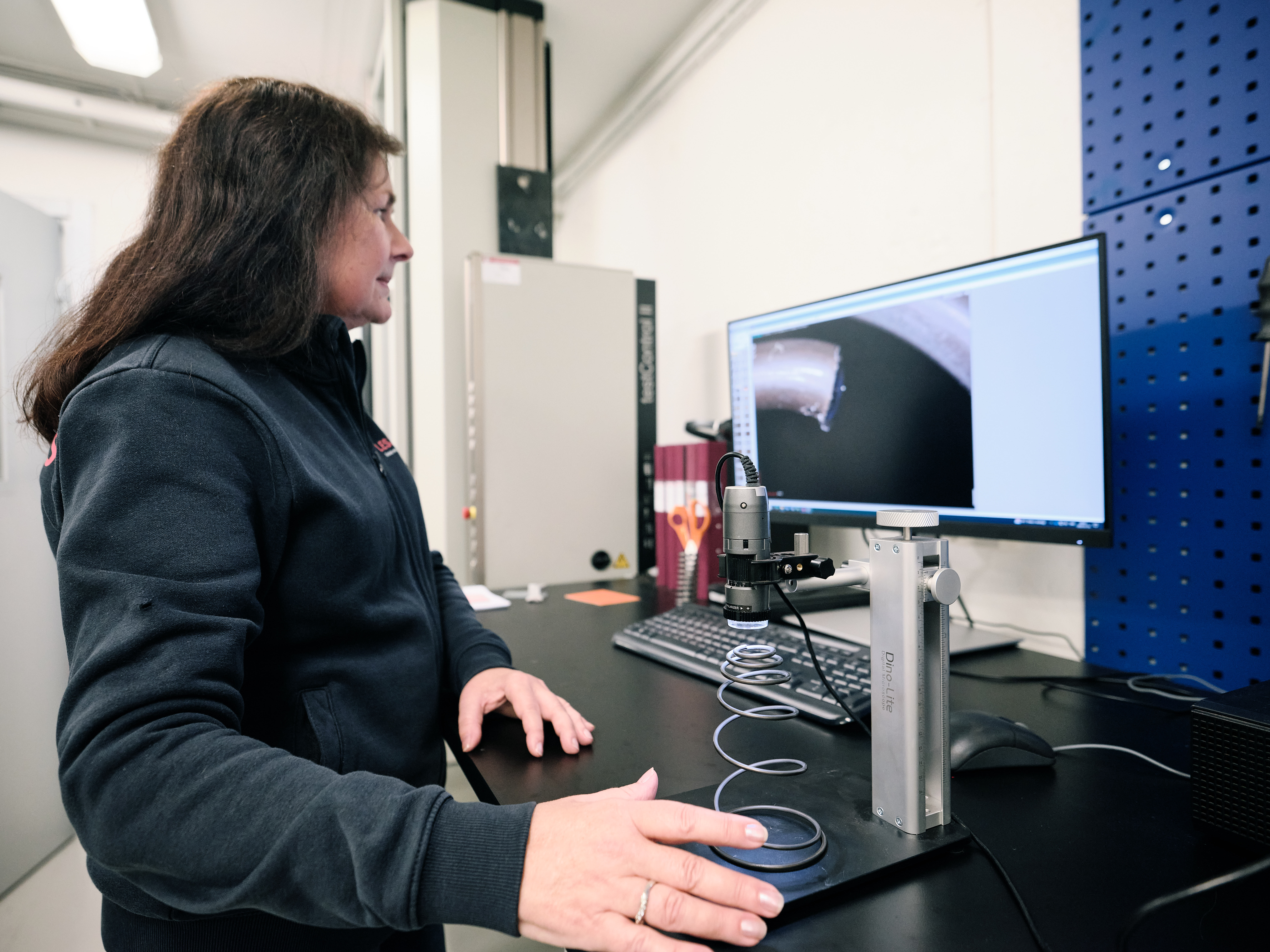 Technician inspecting a conical compression spring under a microscope at a workstation.