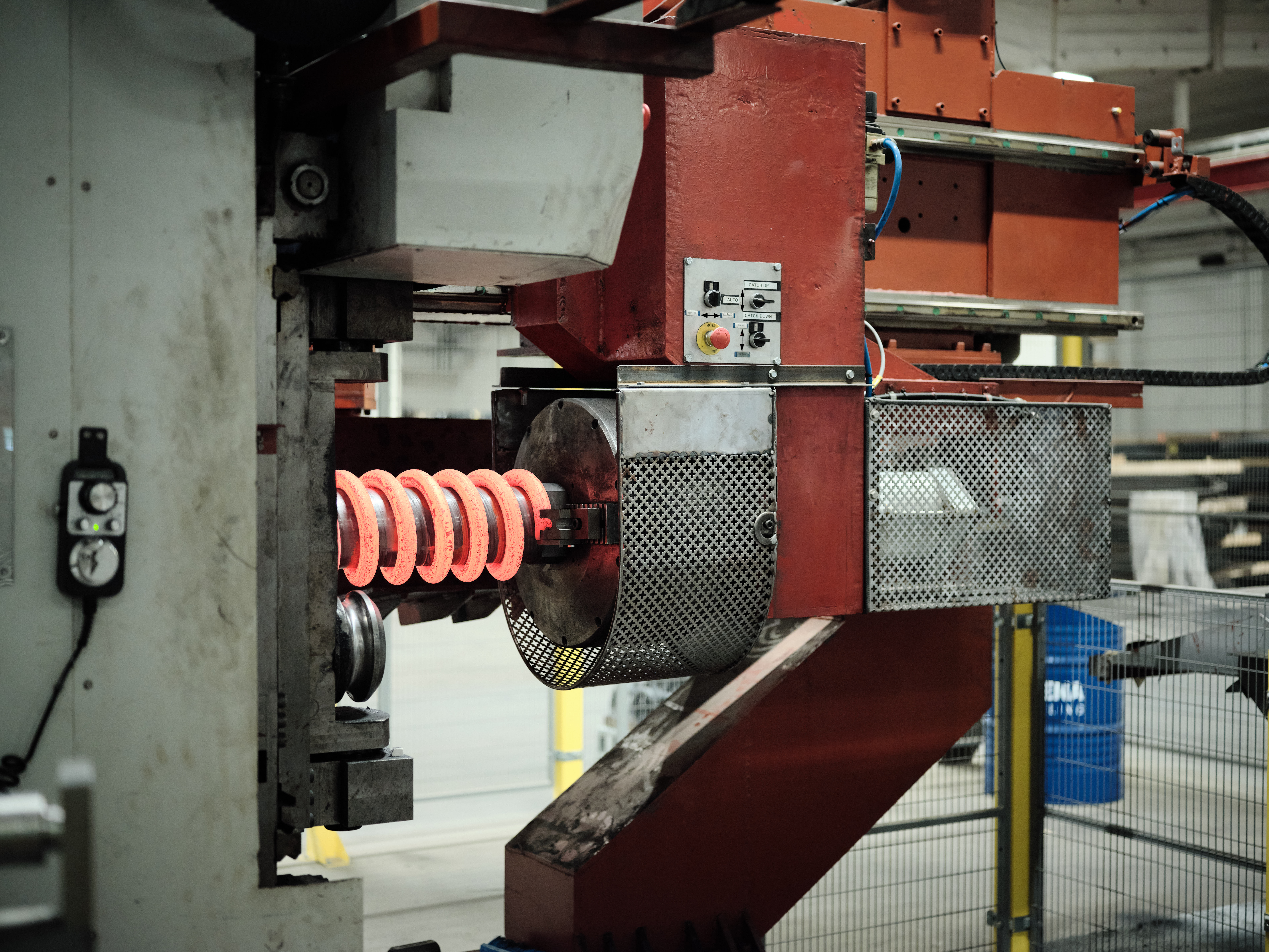 Glowing red-hot compression spring being formed around a metal cylinder in a manufacturing machine.