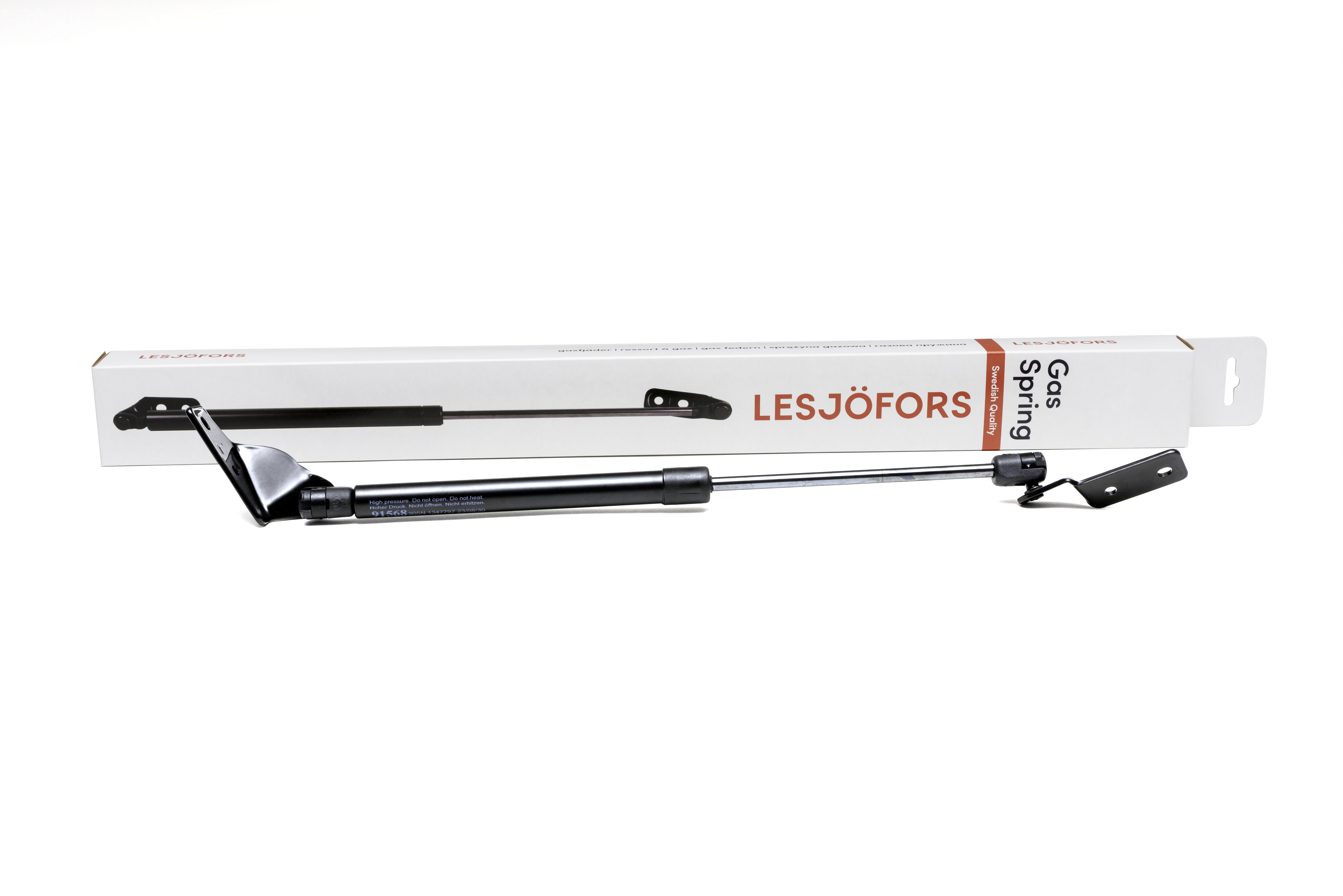 A black and silver gas spring with its packaging behind it, the packaging says “Lesjöfors.” 