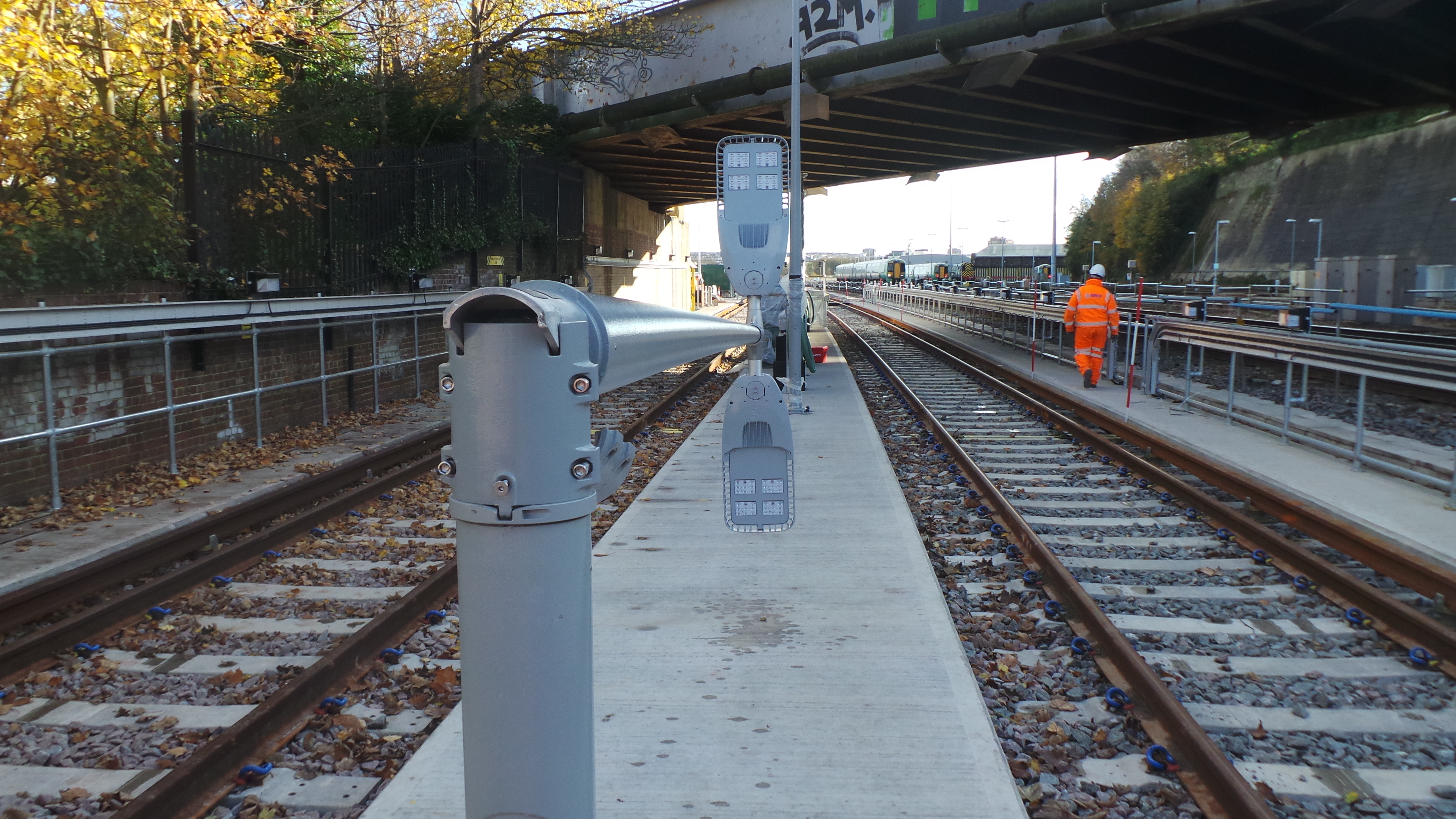 View along train tracks under a bridge with a worker in orange safety gear.