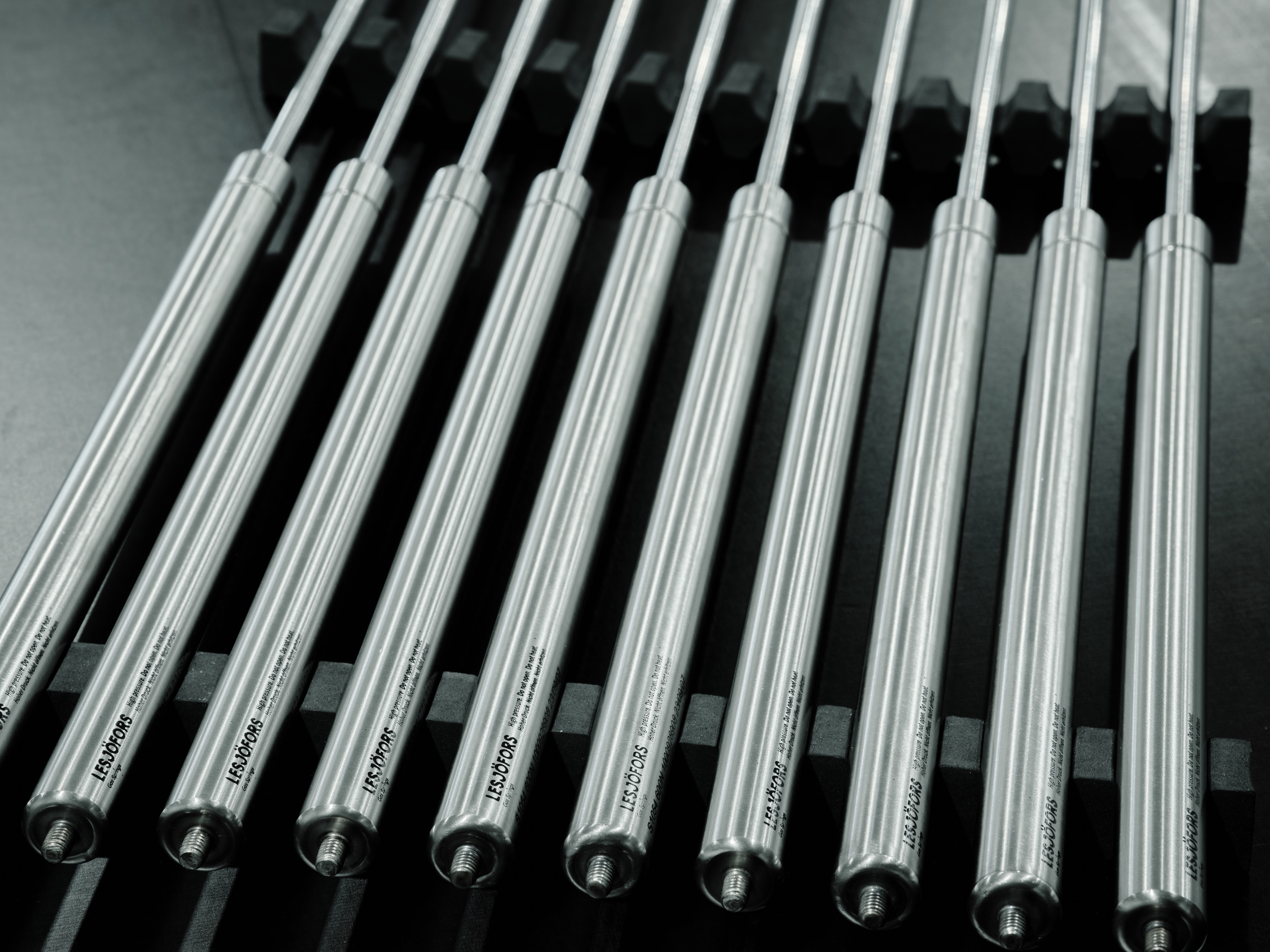 Close-up of silver metal springs arranged in a row, casting soft shadows on a dark surface.