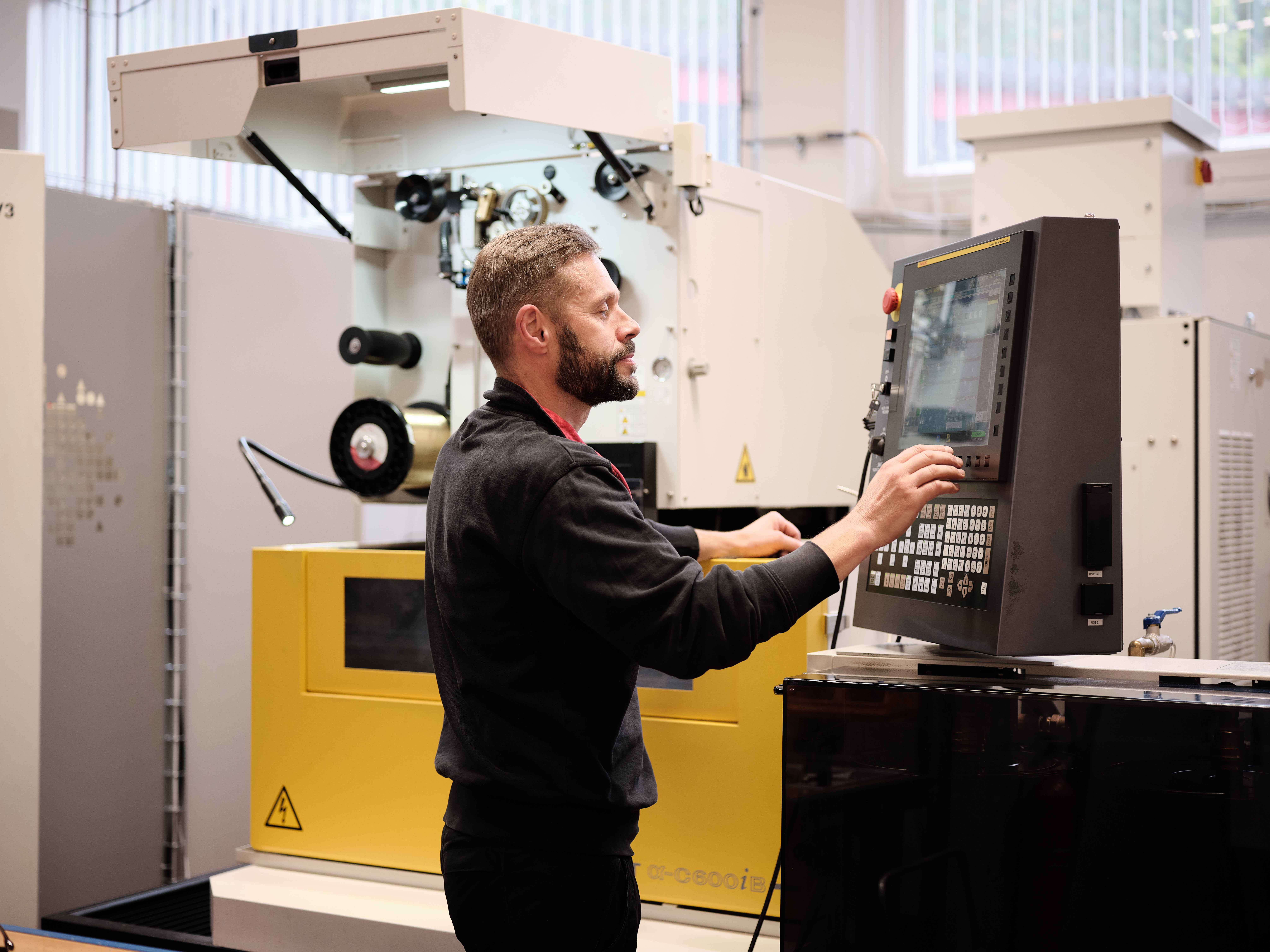 Factory worker operating a CNC machine using a control panel in a workshop.