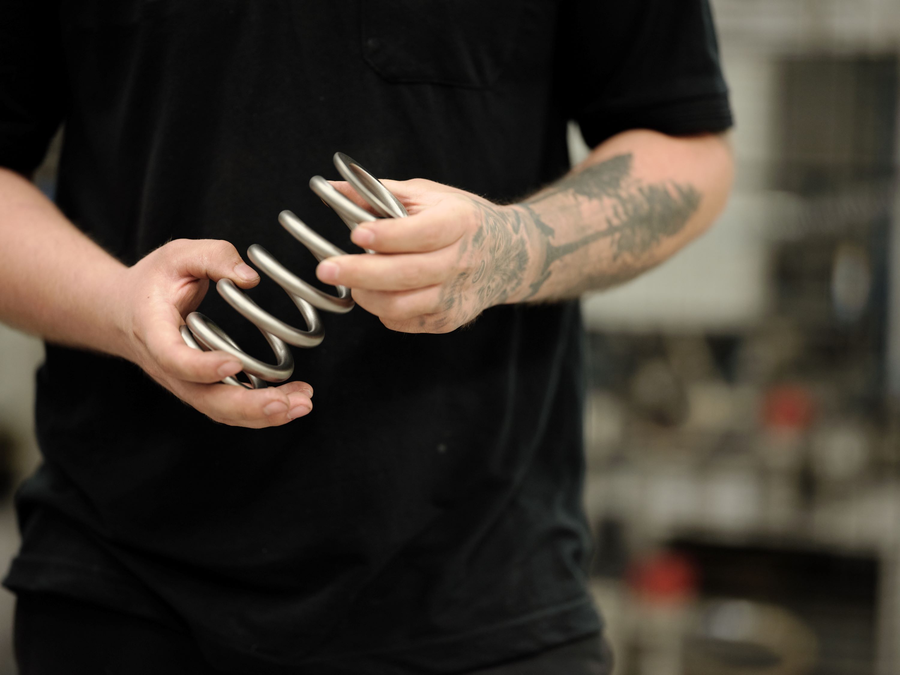 Factory worker holding a large metal coil spring in a workshop.