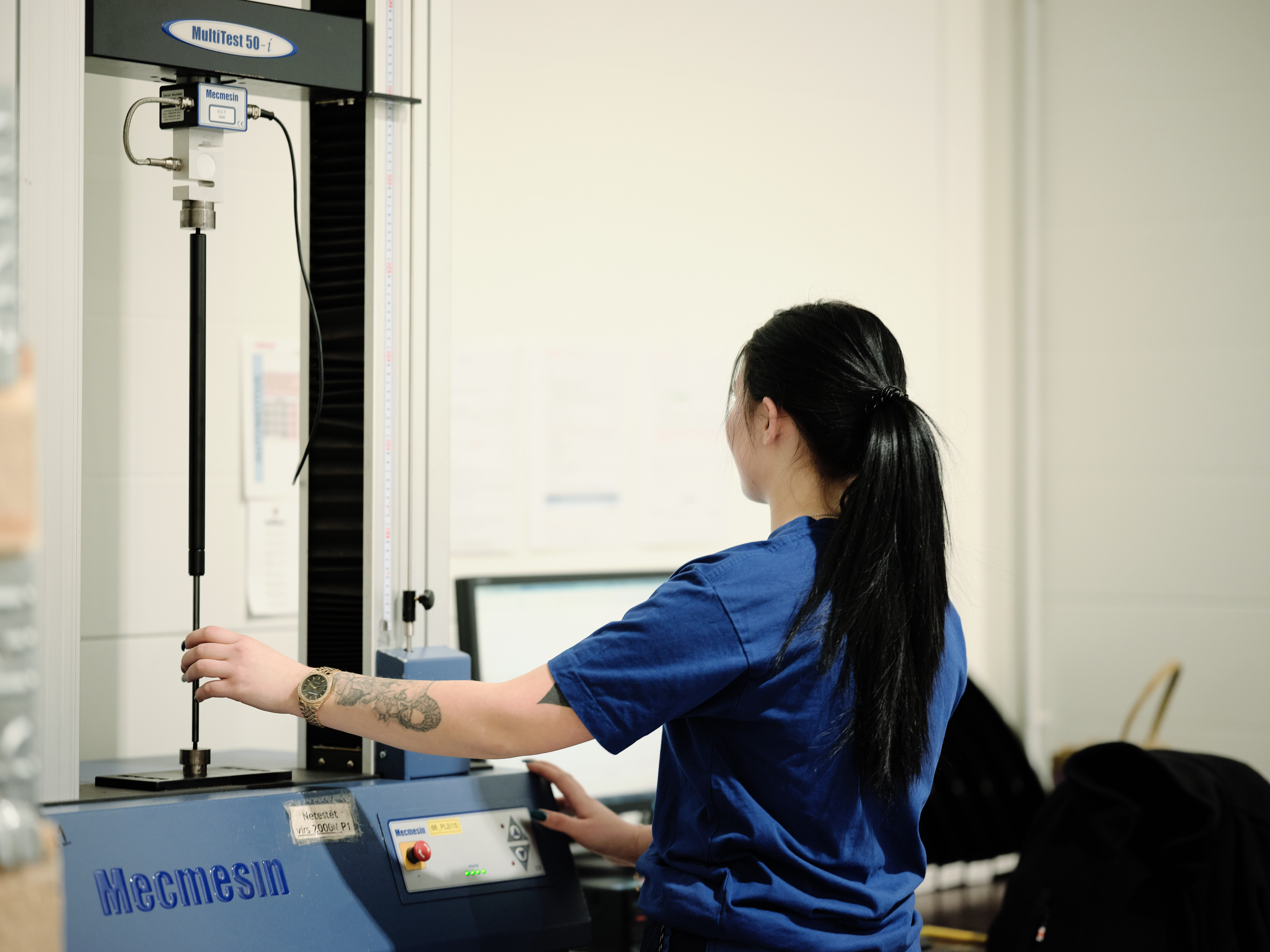 Worker performing a stress test on a long spring on a vertical testing machine.