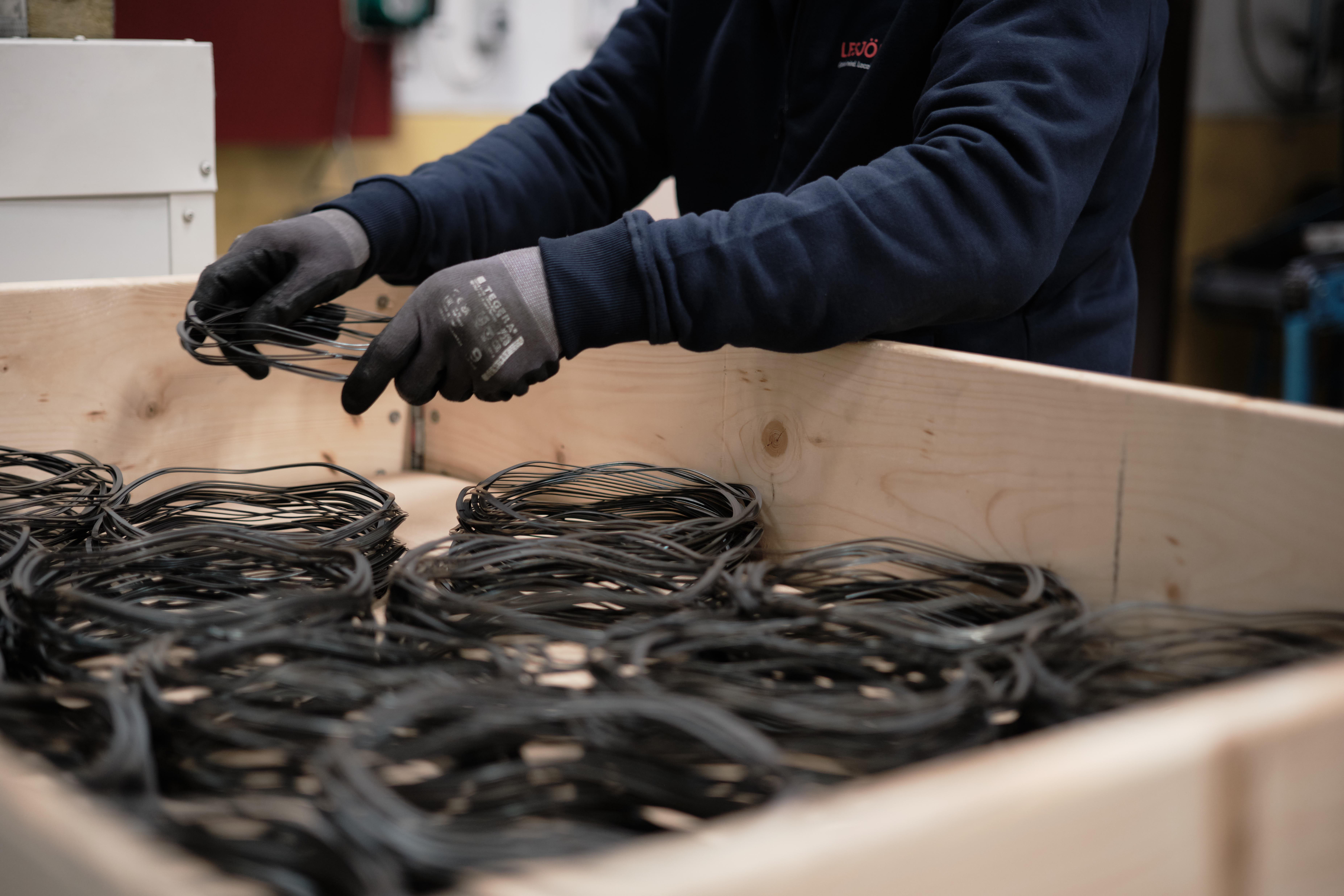 A Lesjöfors factory worker placing stacks of metal wave washers into a wooden crate.