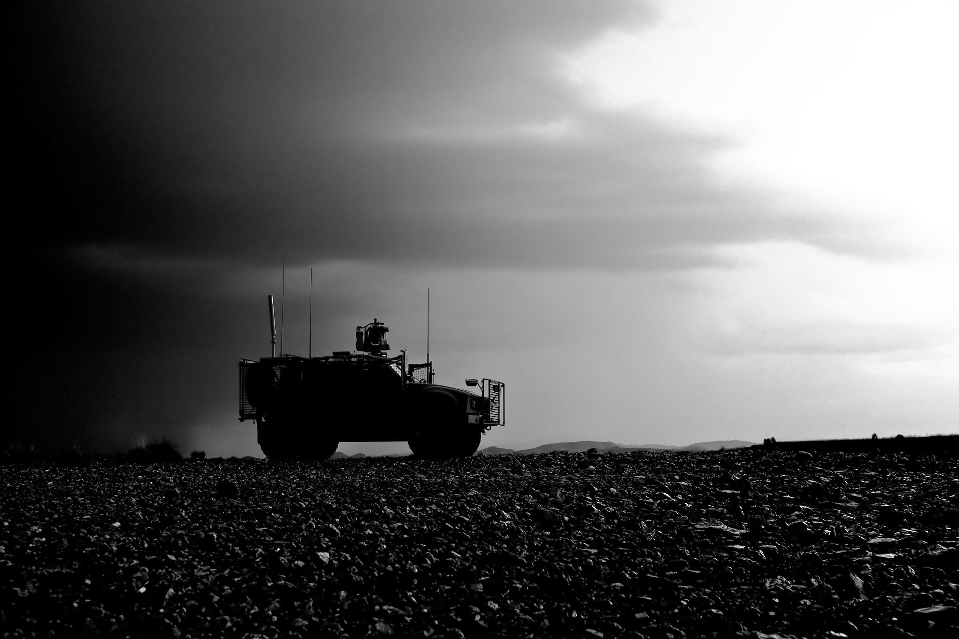 Silhouetted military vehicle on rocky terrain under a dark sky. The contrast of light and dark clouds creates a dramatic view.