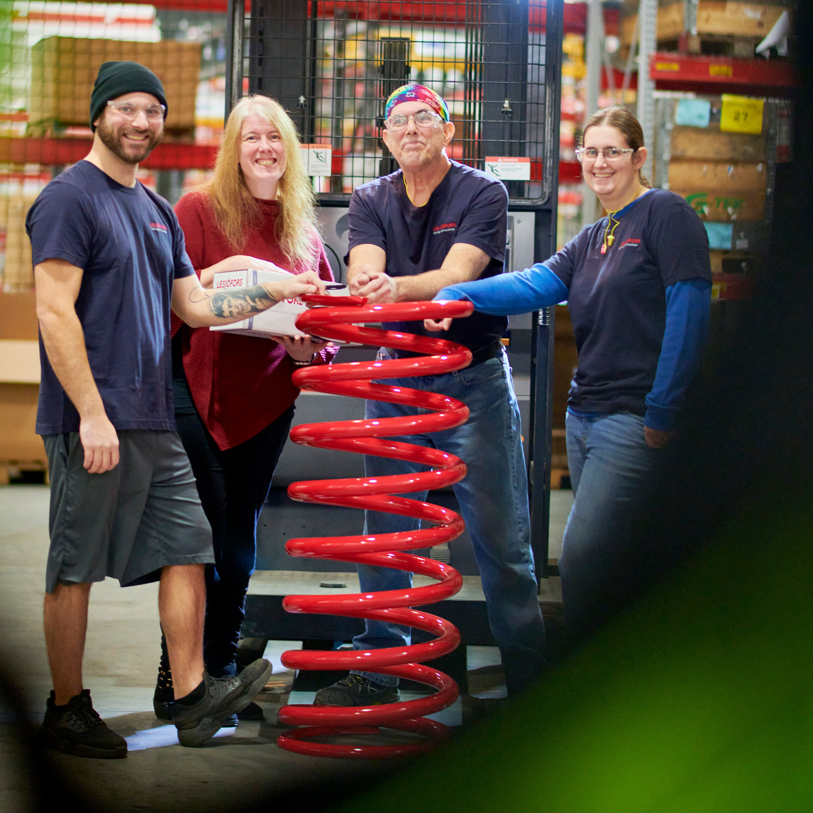 Four Lesjöfors employees posing with a large red coil spring in a warehouse.