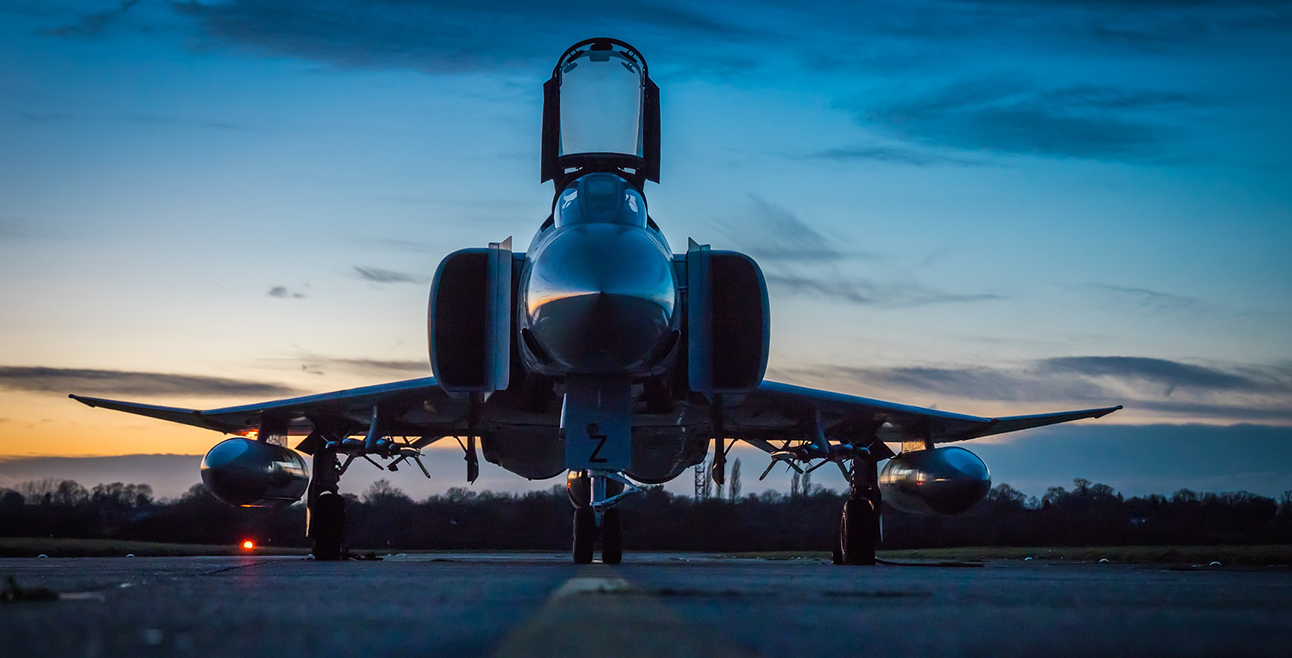 A sleek fighter jet on a runway at dusk under a blue and orange sky.