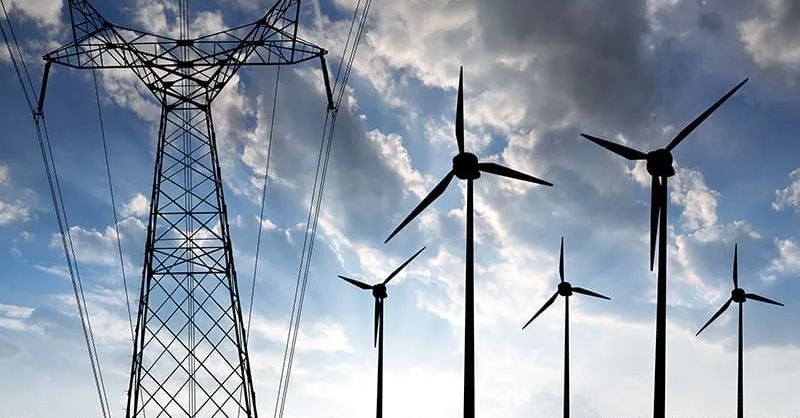 A large electrical transmission tower and several wind turbines stand under a cloudy sky, illustrating sources and distribution of electrical energy.
