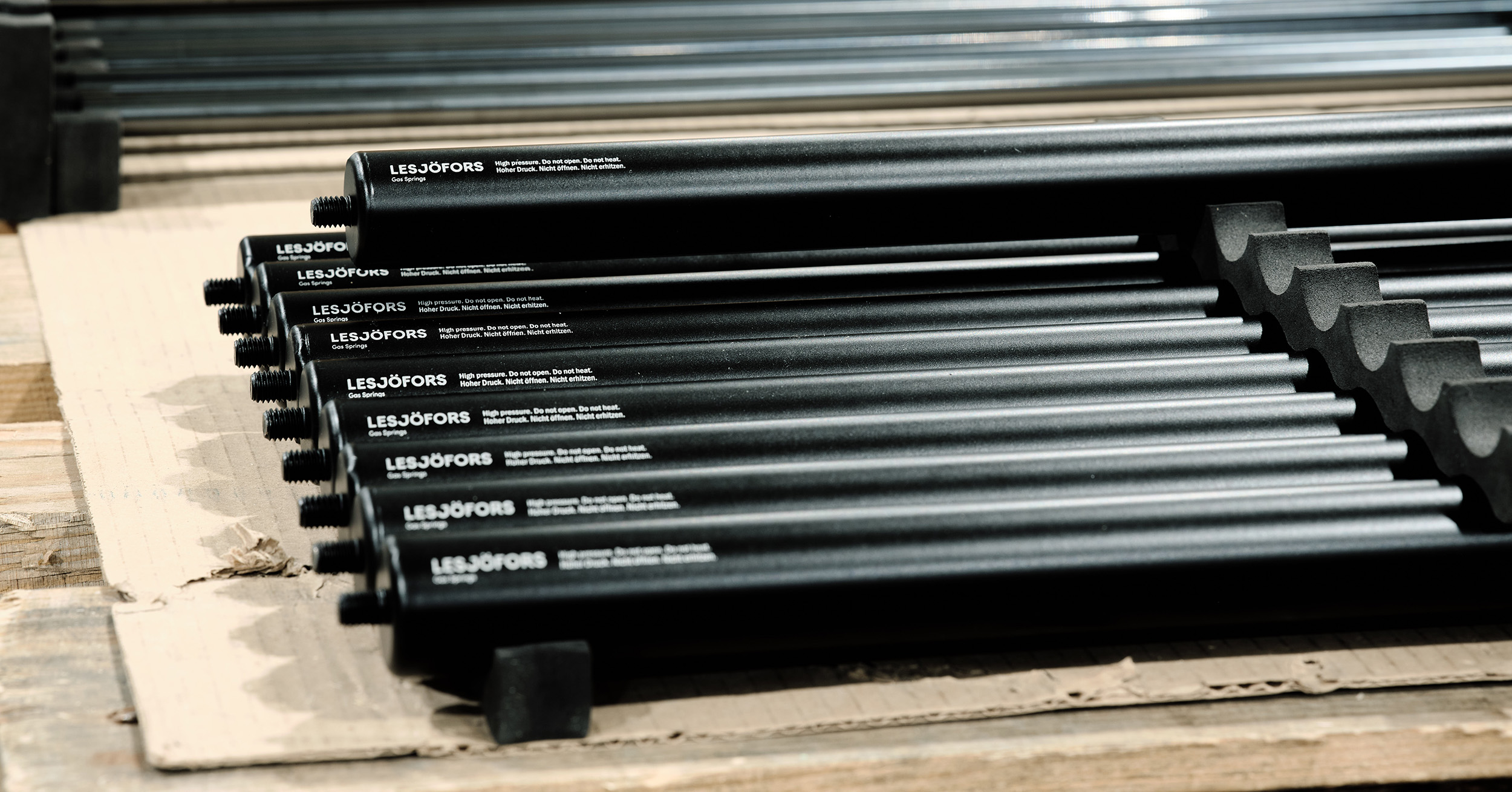 Rows of black Lesjöfors gas springs arranged on a cardboard surface, with the brand name visible on the casing.