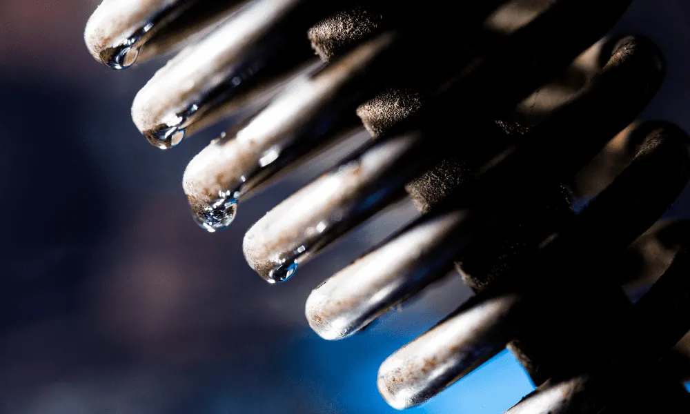 Close-up of water droplets forming on the tips of a compressions spring, with a blurred blue background.