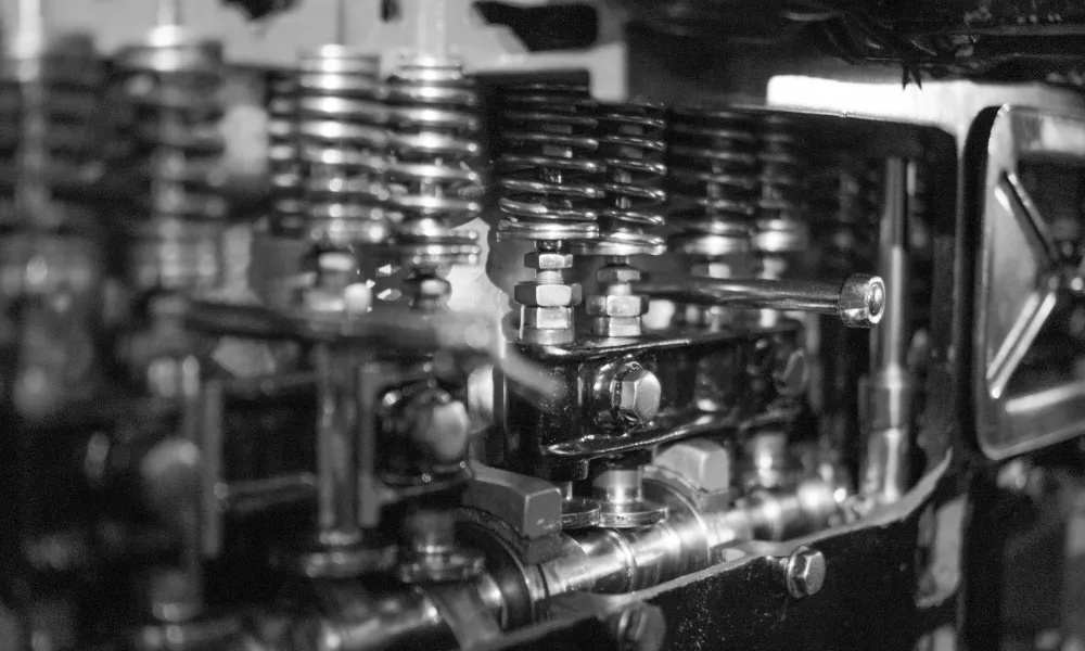 A black and white close-up photograph of a mechanical engine showing multiple compression springs and valve components in a row.