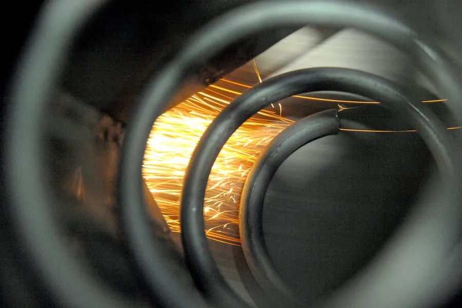 Sparks flying as a metal compression spring is ground on a coil grinder.