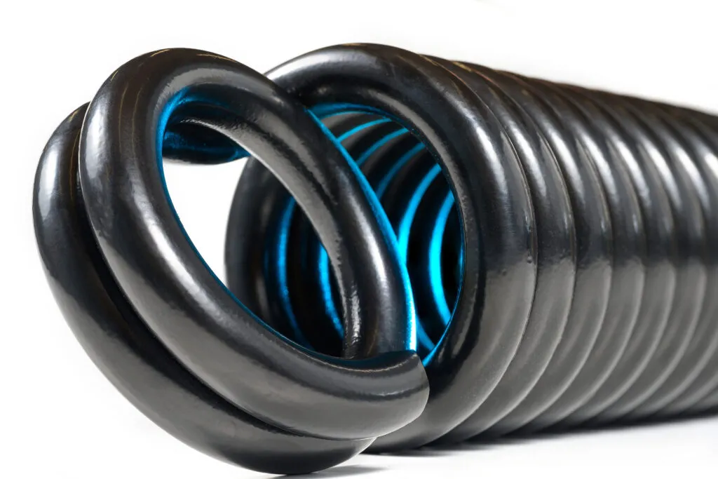 Close-up of a large black tension spring with a circular loop end, revealing vivid blue reflections inside the tightly wound coils, against a white background