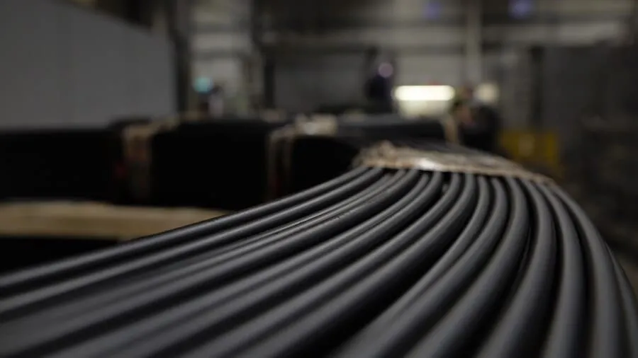 Close-up of multiple curved metal rods aligned in parallel, with a blurred factory environment in the background.