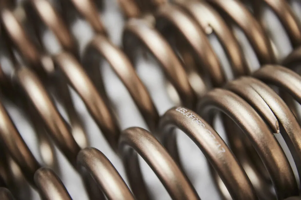 Close-up of bronze-colored metal coil springs lined up, with the Lesjöfors brand name printed on the surface.