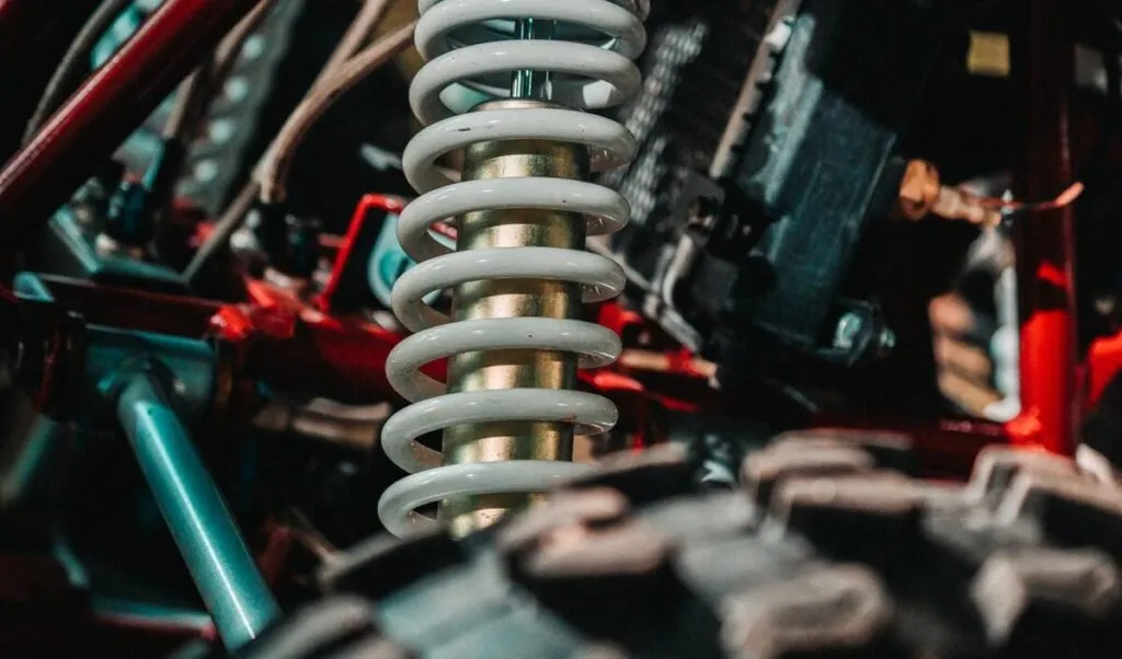 Close-up of off-road vehicle suspension with white coil spring and rugged components.