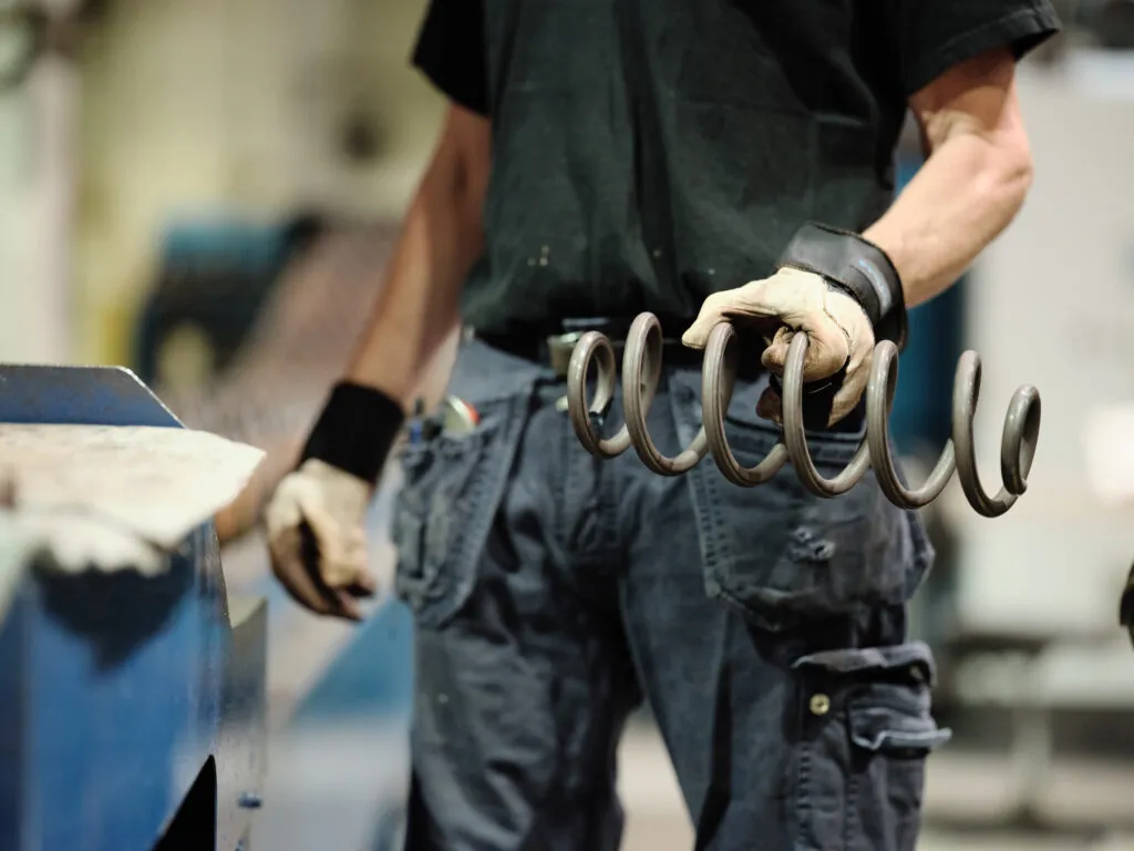 Lesjöfors factory worker in gloves holding a set of banana springs in an industrial manufacturing environment.