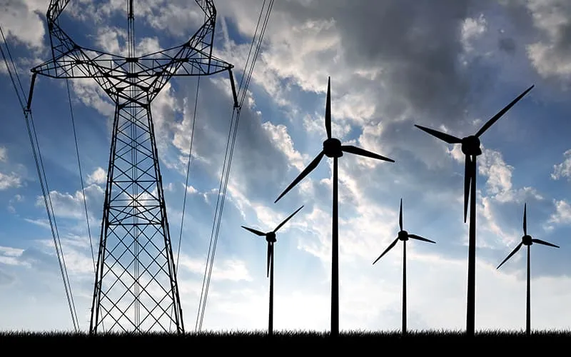 Wind turbines beside an electricity transmission tower against a cloudy sky.