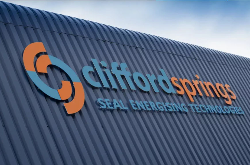 Sign for Cliffsprings logo on a corrugated metal wall. Blue and orange text reads, “Clifford Springs - your logistics partner.” Sky visible above.