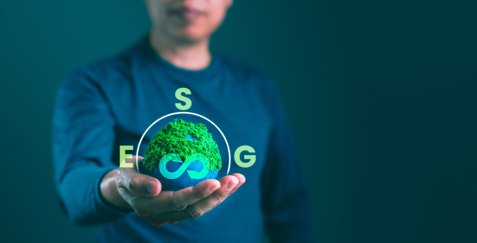 A person in a blue shirt holds a glowing green earth with an infinity symbol, surrounded by the letters E, S, G, symbolizing sustainability.