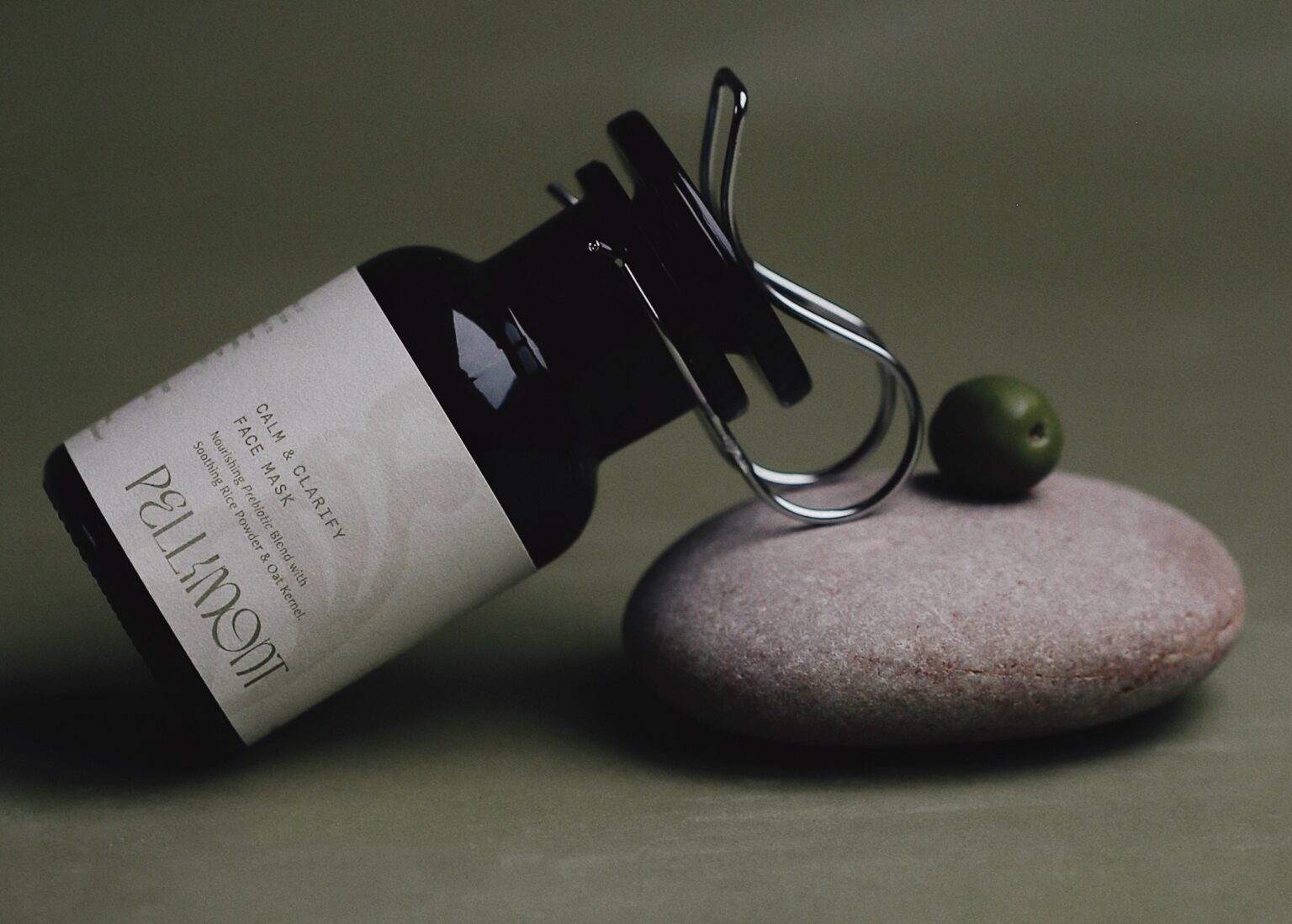 A dark amber glass bottle with a dropper lies on a smooth, round stone against a muted green background, evoking a sense of tranquility and natural simplicity.