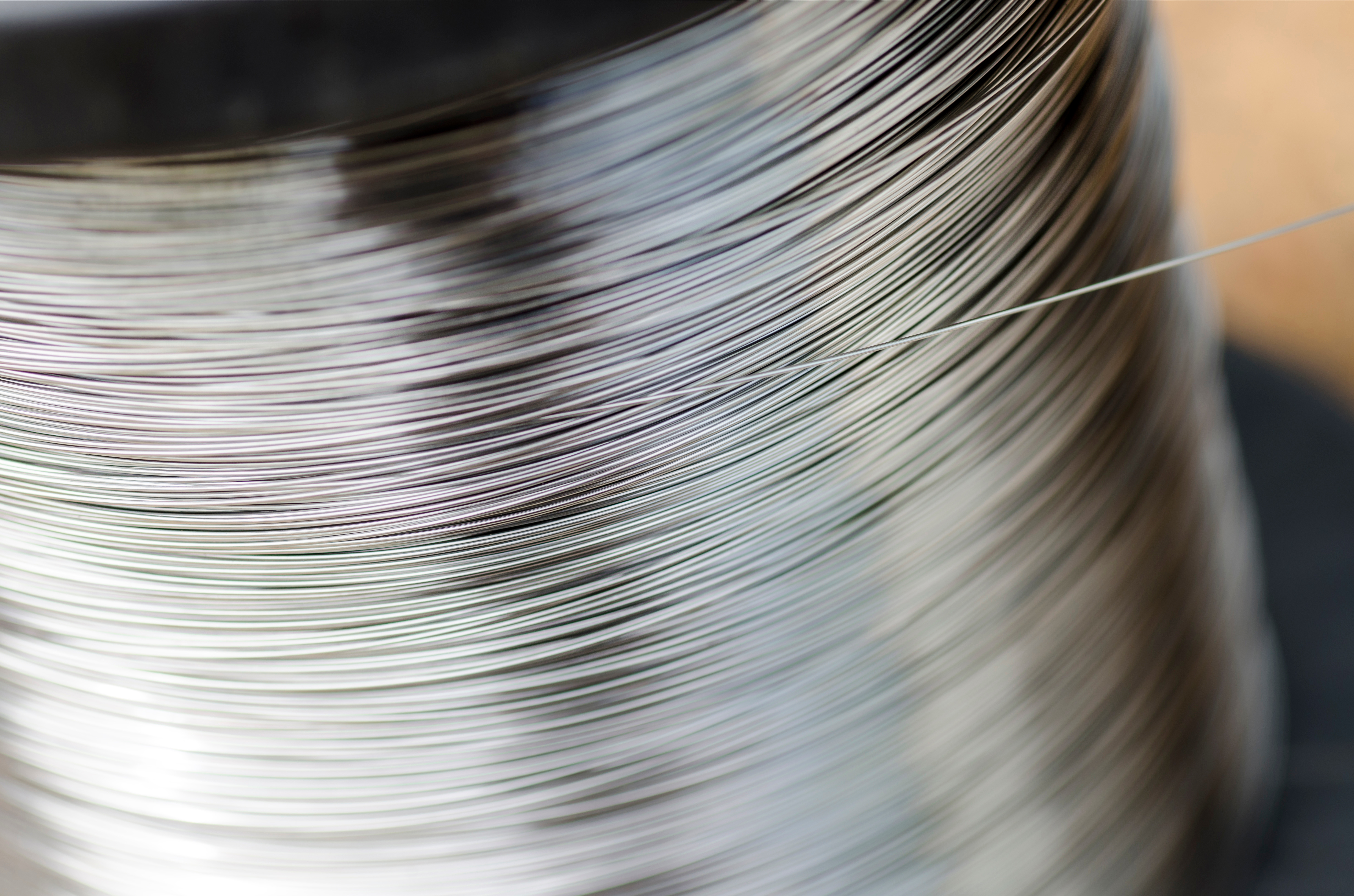 Close-up of a spinning reel of shiny, metallic thread. The blurred motion creates a dynamic and textured pattern.