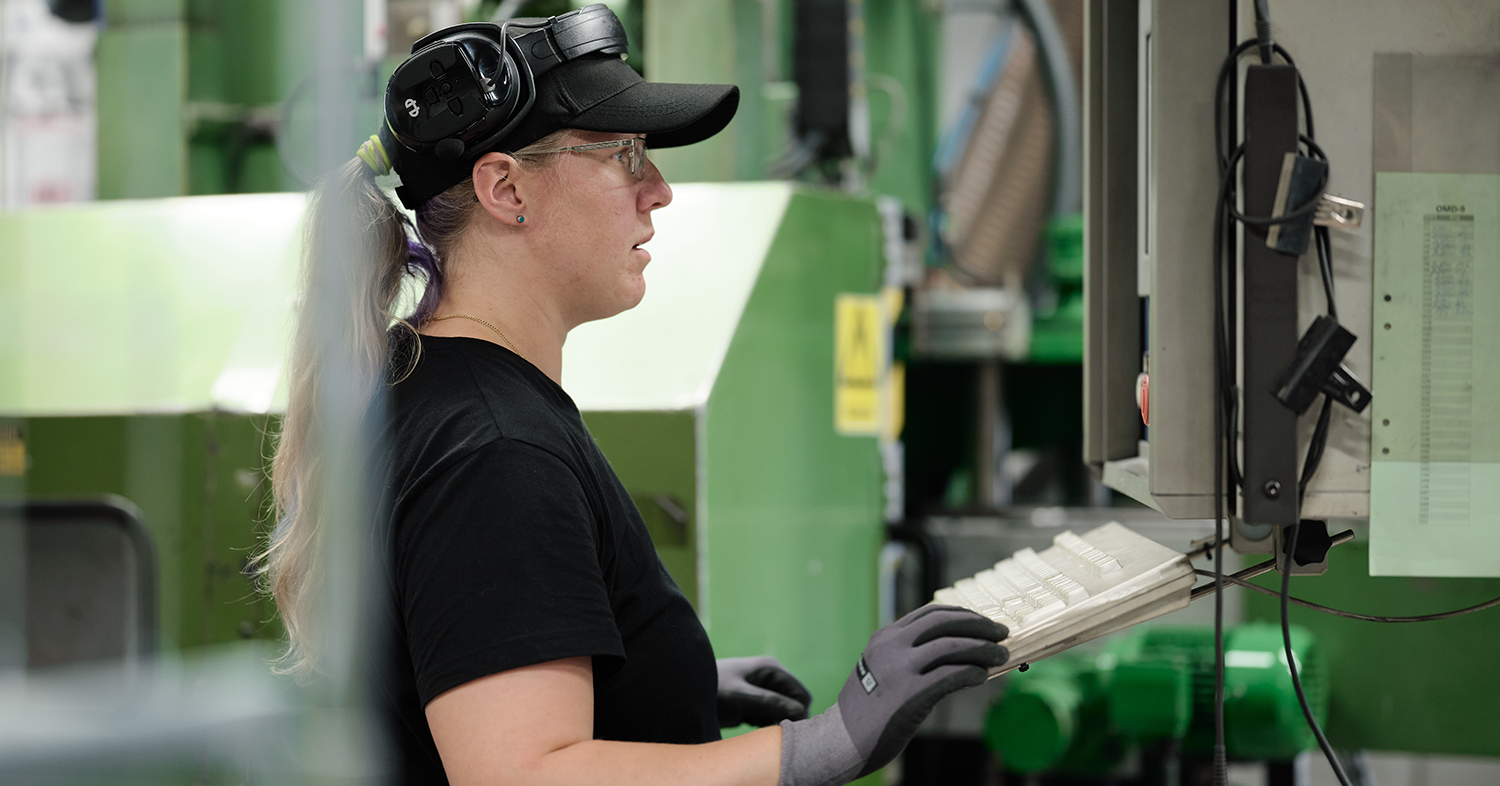 A person wearing a black cap and safety goggles operates machinery in an industrial setting.