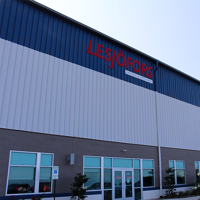 Industrial building facade with blue and gray panels; large red "LESJÖFORS Springs & Pressings" sign on top.