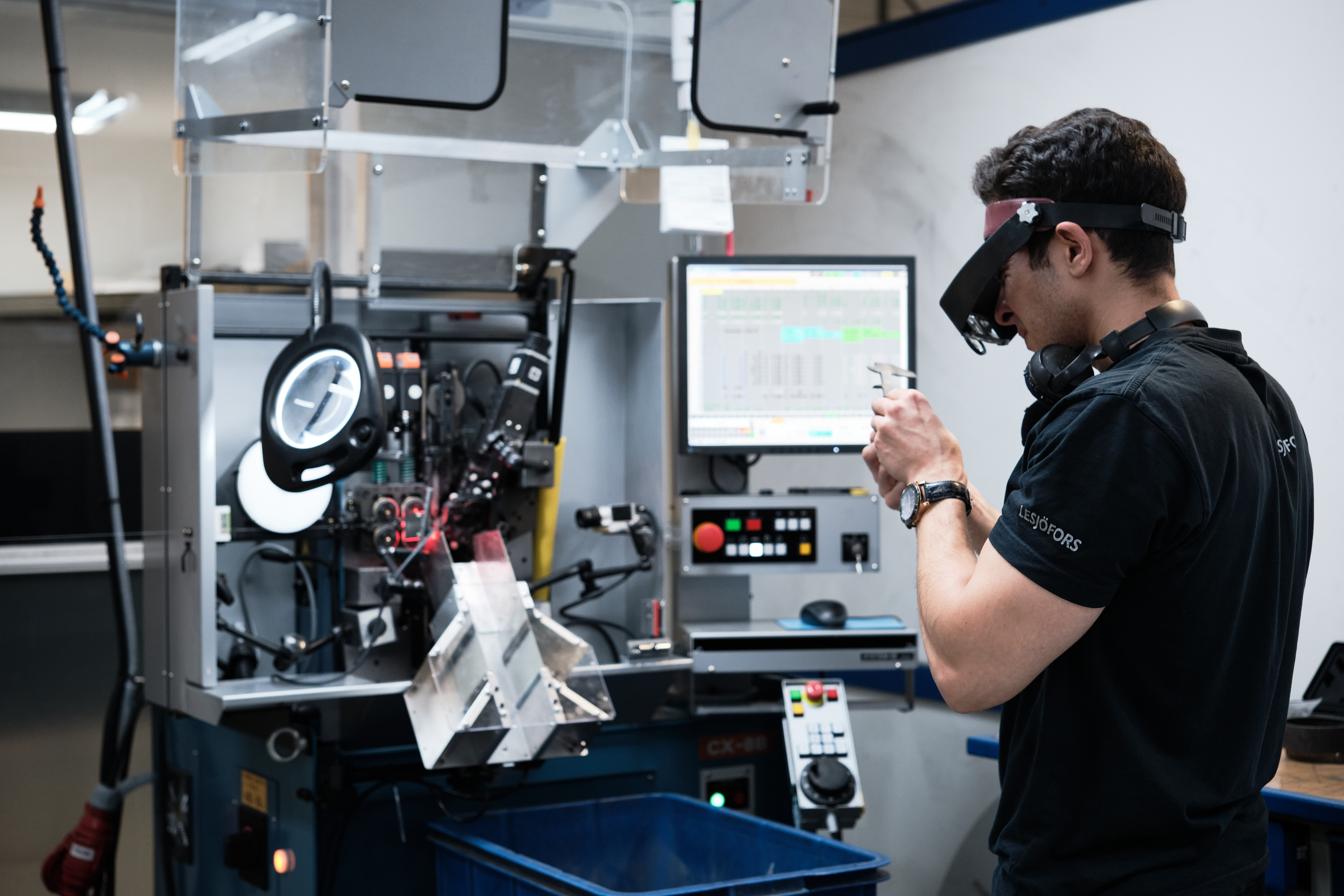 A lesjöfors factory worker inspecting a small metal part at a precision manufacturing machine.