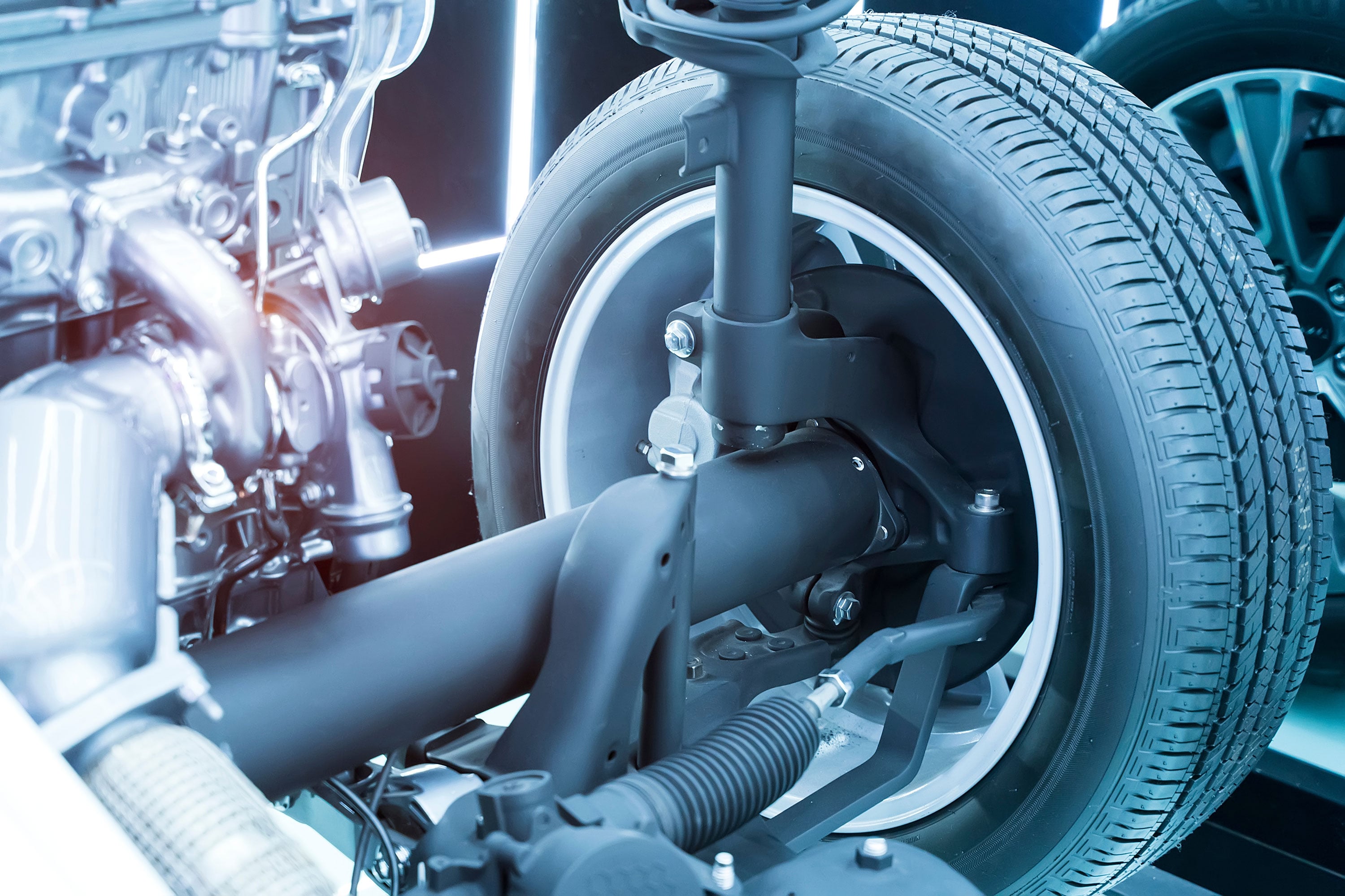 A close-up of a vehicle suspension system showing the tire, shock absorber, spring, and metal components.