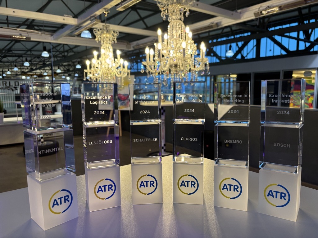 Six awards with a logo displayed, set on a table in an elegant space with chandeliers and industrial-style windows, creating a formal atmosphere.