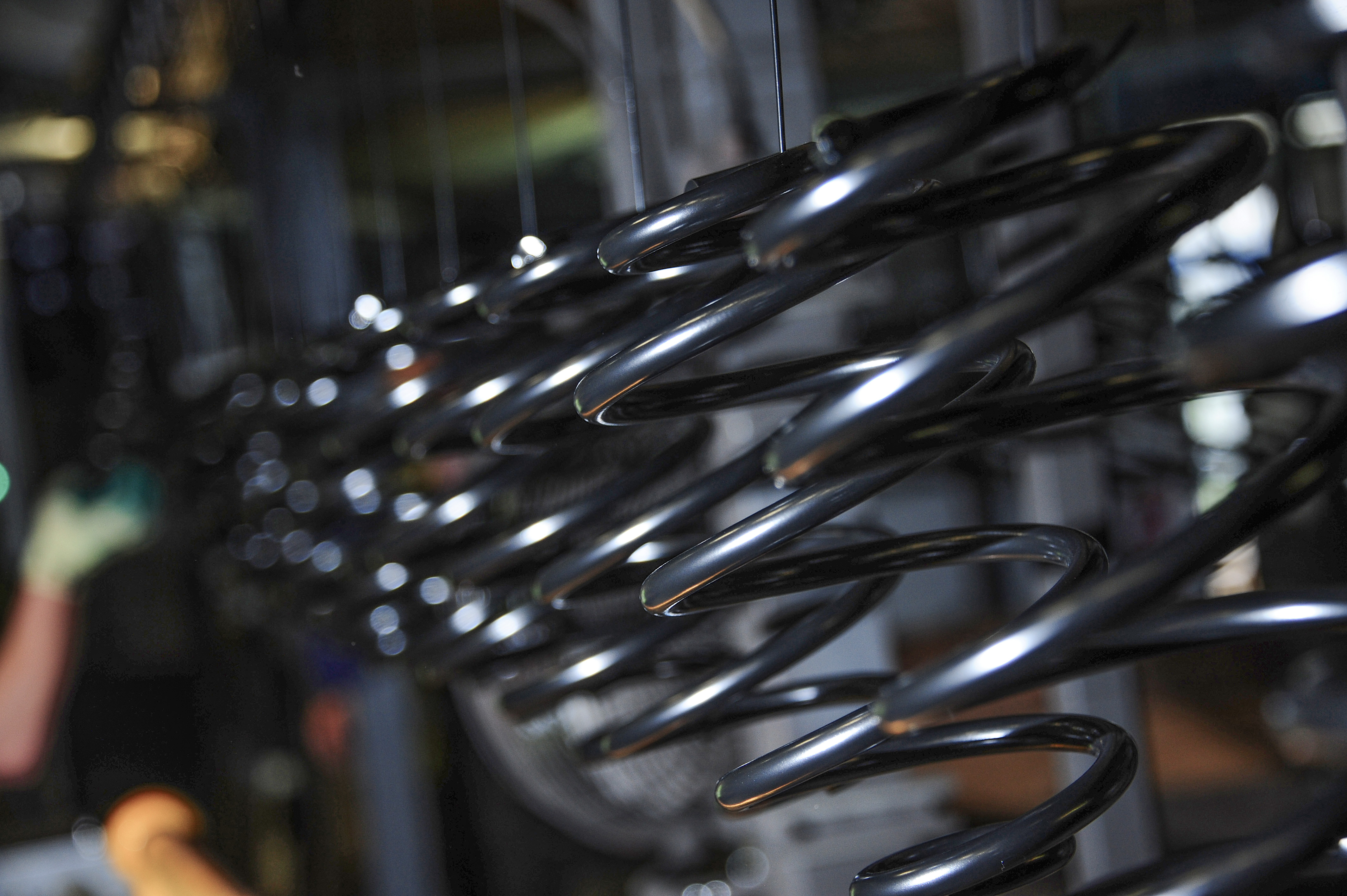 Close-up of shiny black metal coilsprings in a factory setting, with soft-focus background showing industrial machinery and a worker. 
