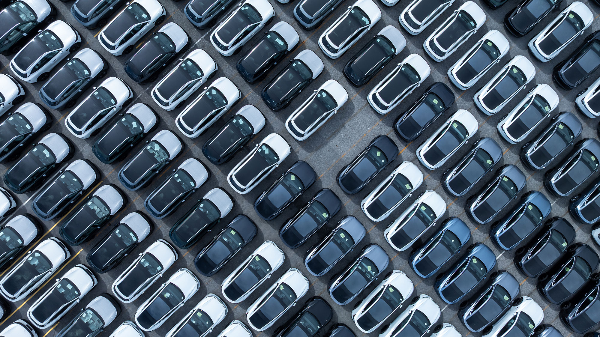 Aerial view of rows of newly manufactured cars parked in parallel lines, with one empty space.