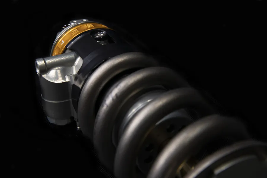 Close-up of a motorcycle shock absorber with coil spring and damping adjuster.