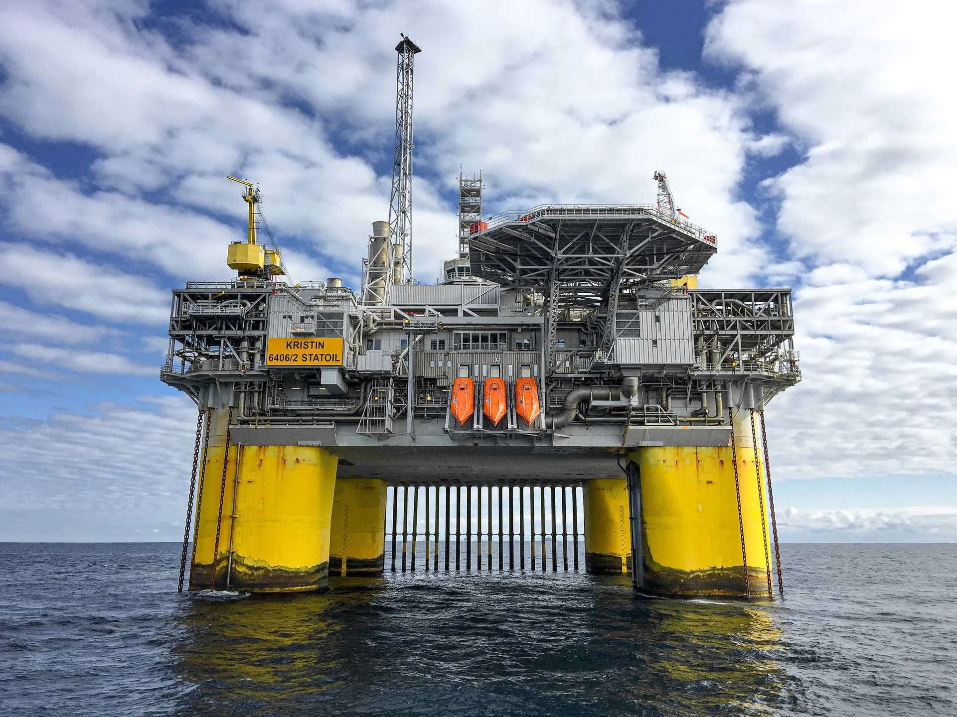 Offshore oil and gas production platform supported by large yellow columns at sea.