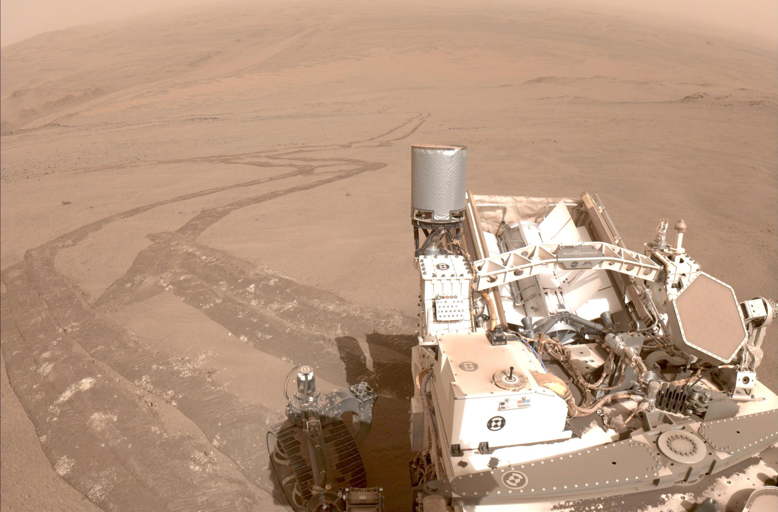 NASA's Perseverance rover on the surface of Mars with its tracks extending across the landscape.
