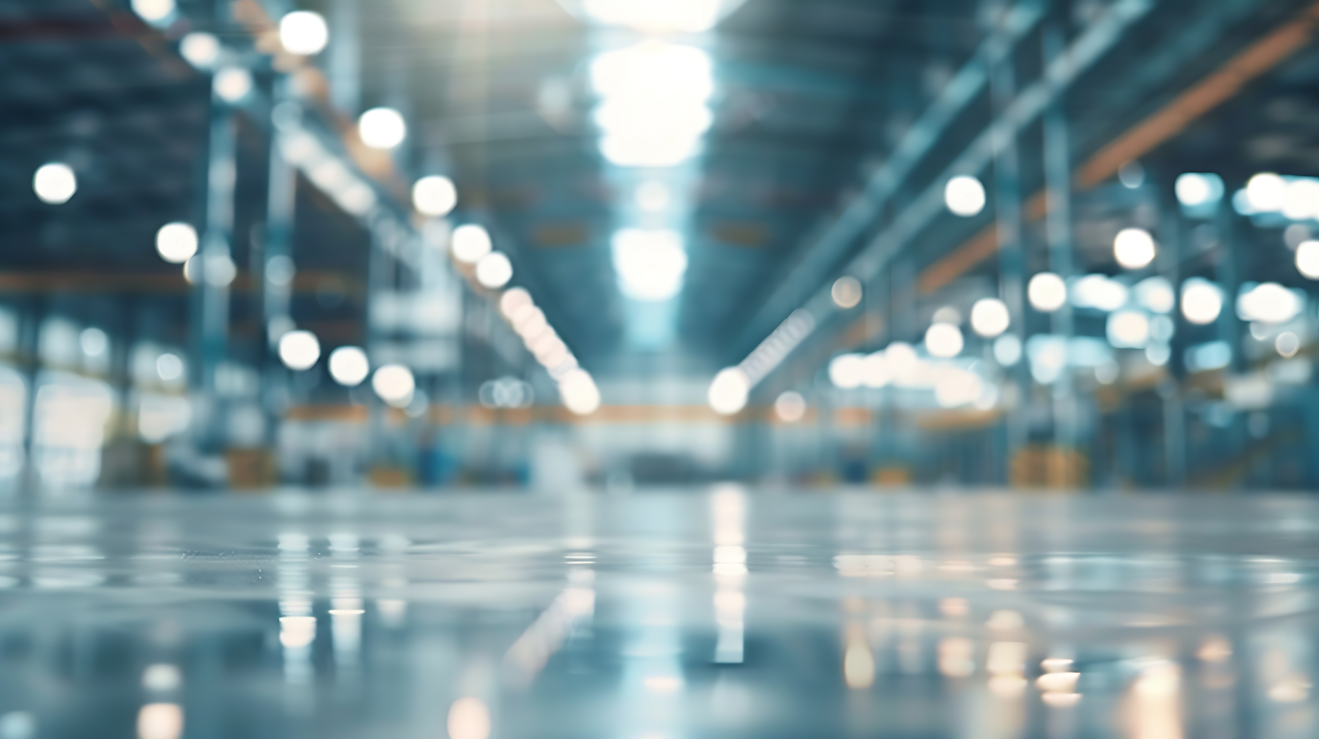 Blurred image of a large, empty warehouse with reflective flooring and bright overhead lights. 