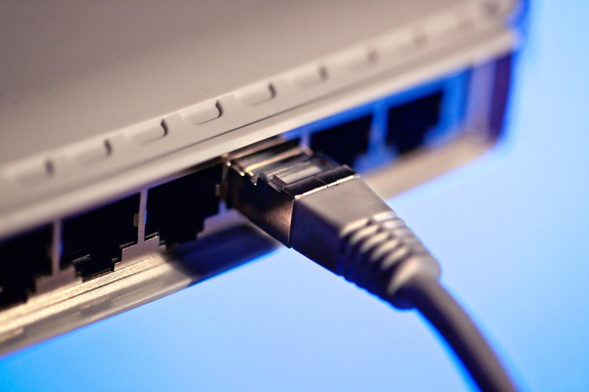 Close-up of a black Ethernet cable plugged into a network switch, with a blue background. 
