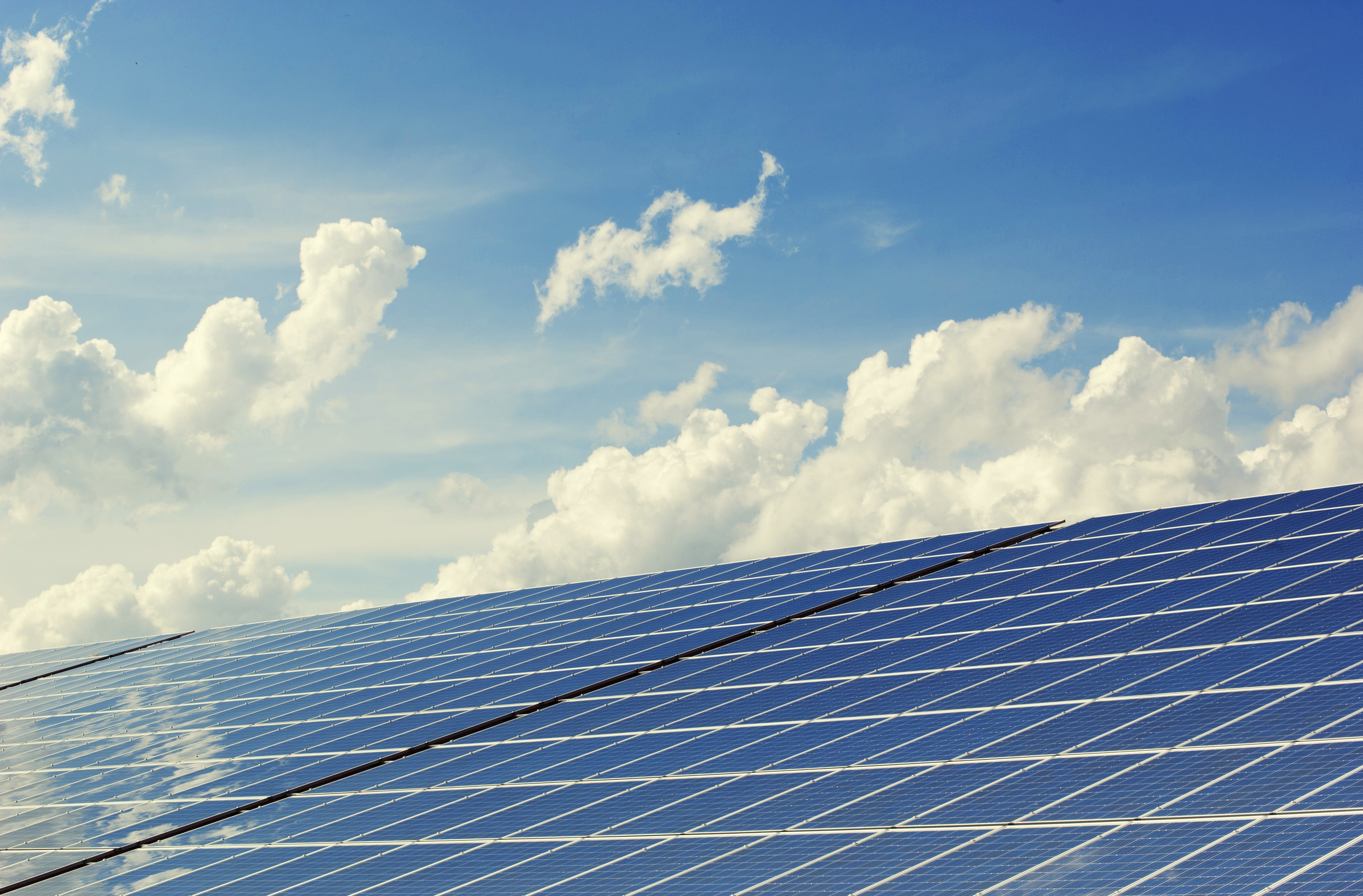 Solar panels reflecting sunlight under a clear blue sky with scattered clouds.