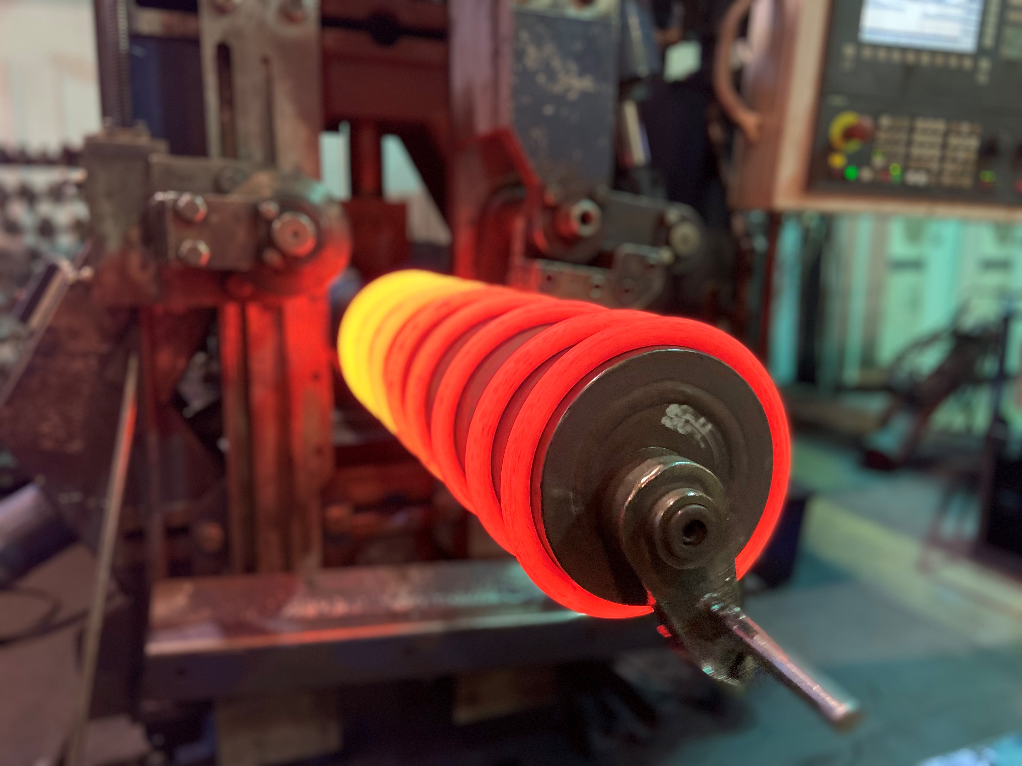 A machine processes a metal spring glowing bright red from heat, signifying high-temperature treatment in an industrial setting.