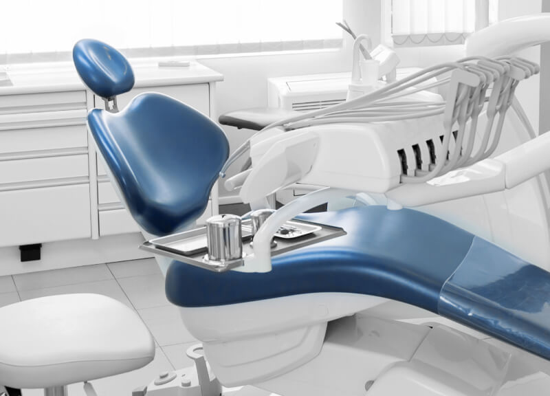 A modern dental office with a blue dental chair, white equipment, and light-filled environment.