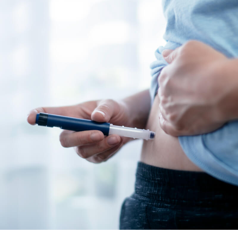 A person using a pen injector to administer an insulin injection into their abdomen.
