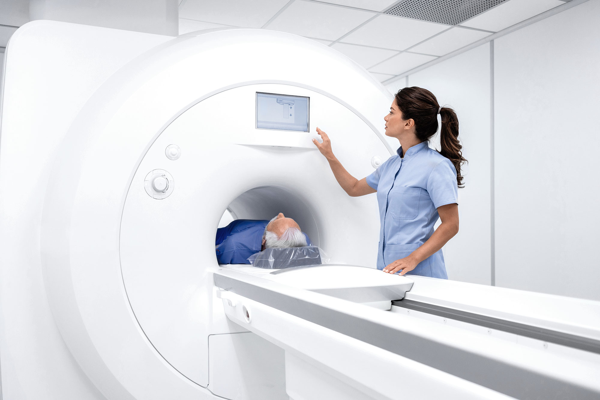 A healthcare professional operates an MRI machine as a patient lies inside. The setting is clinical, emphasizing precision and care in a hospital environment.