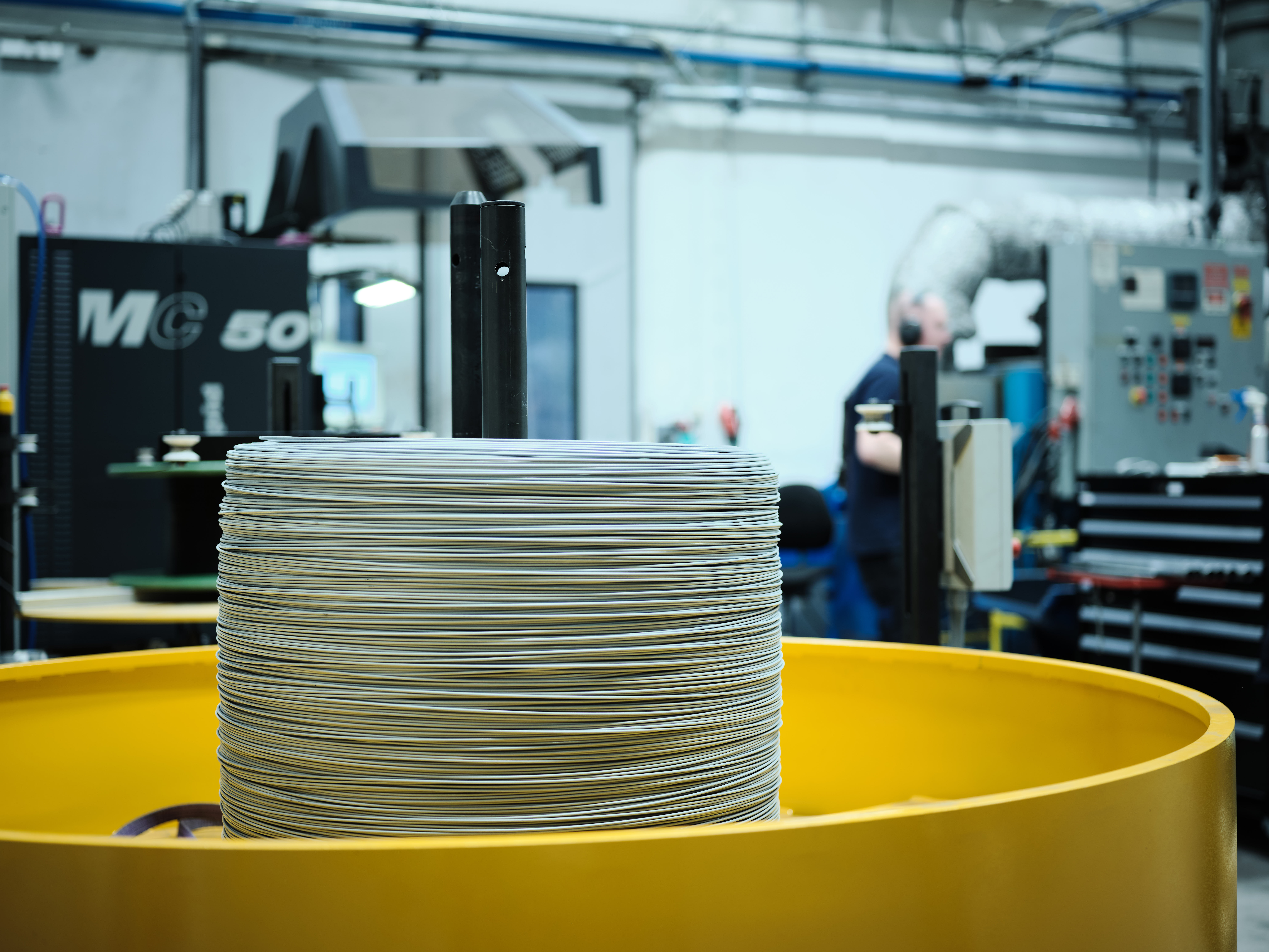 Large spool of white thread in a yellow holder in a factory setting. Industrial equipment and a person in the background