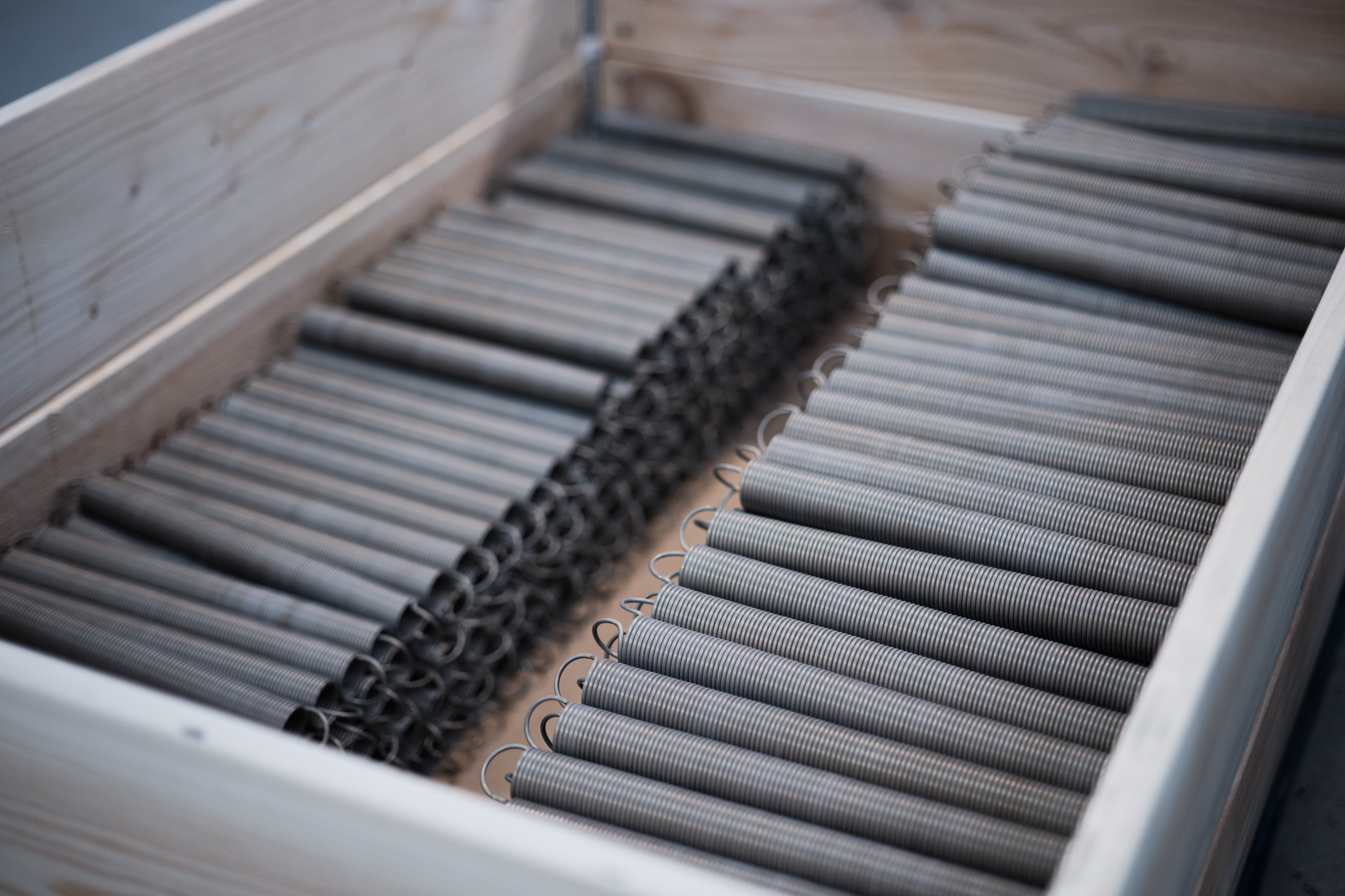 A wooden box with neatly arranged gray tension springs and a black mesh-like divider.