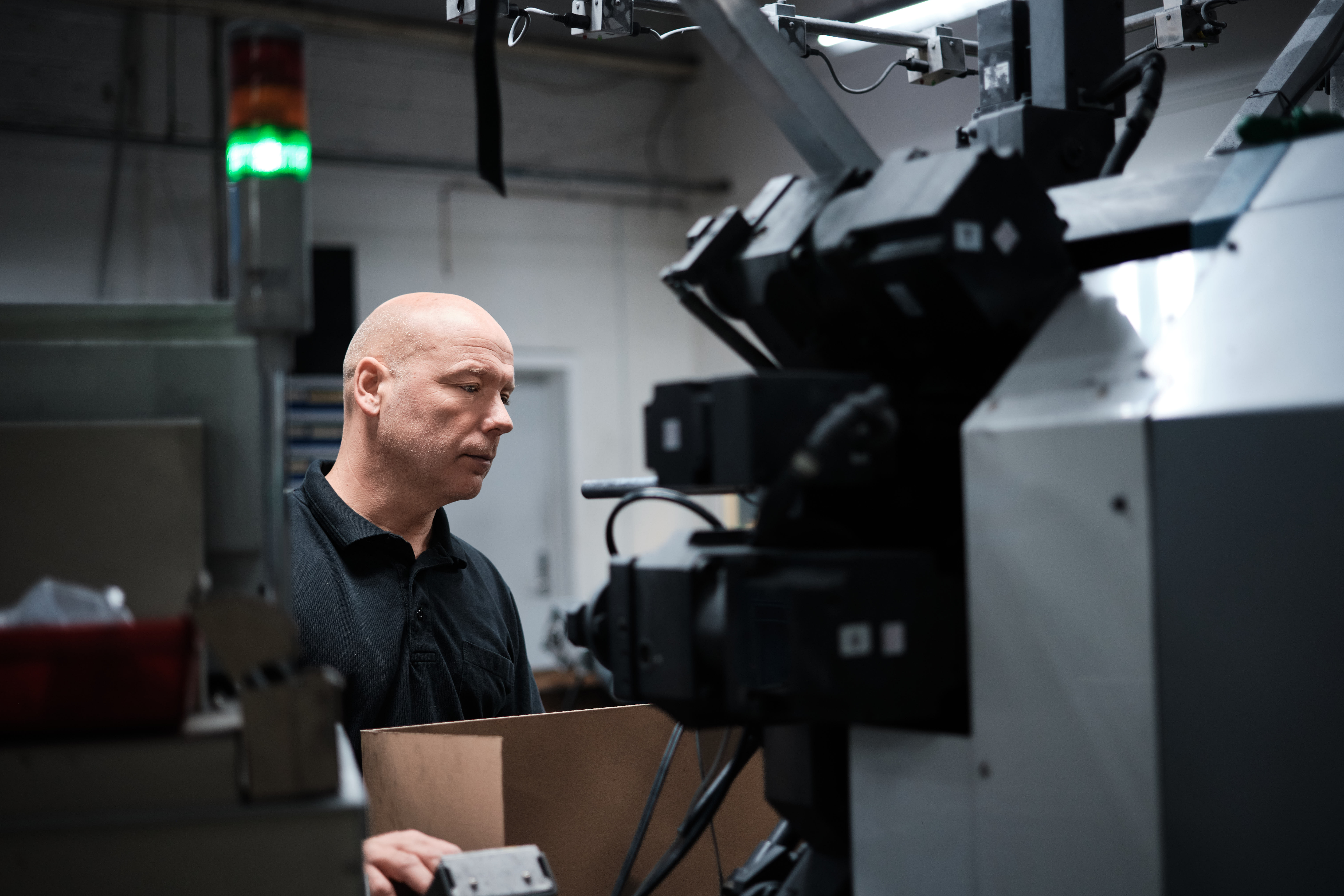 A focused man operates a large industrial machine in a dimly lit factory, conveying concentration and precision in a high-tech manufacturing setting.