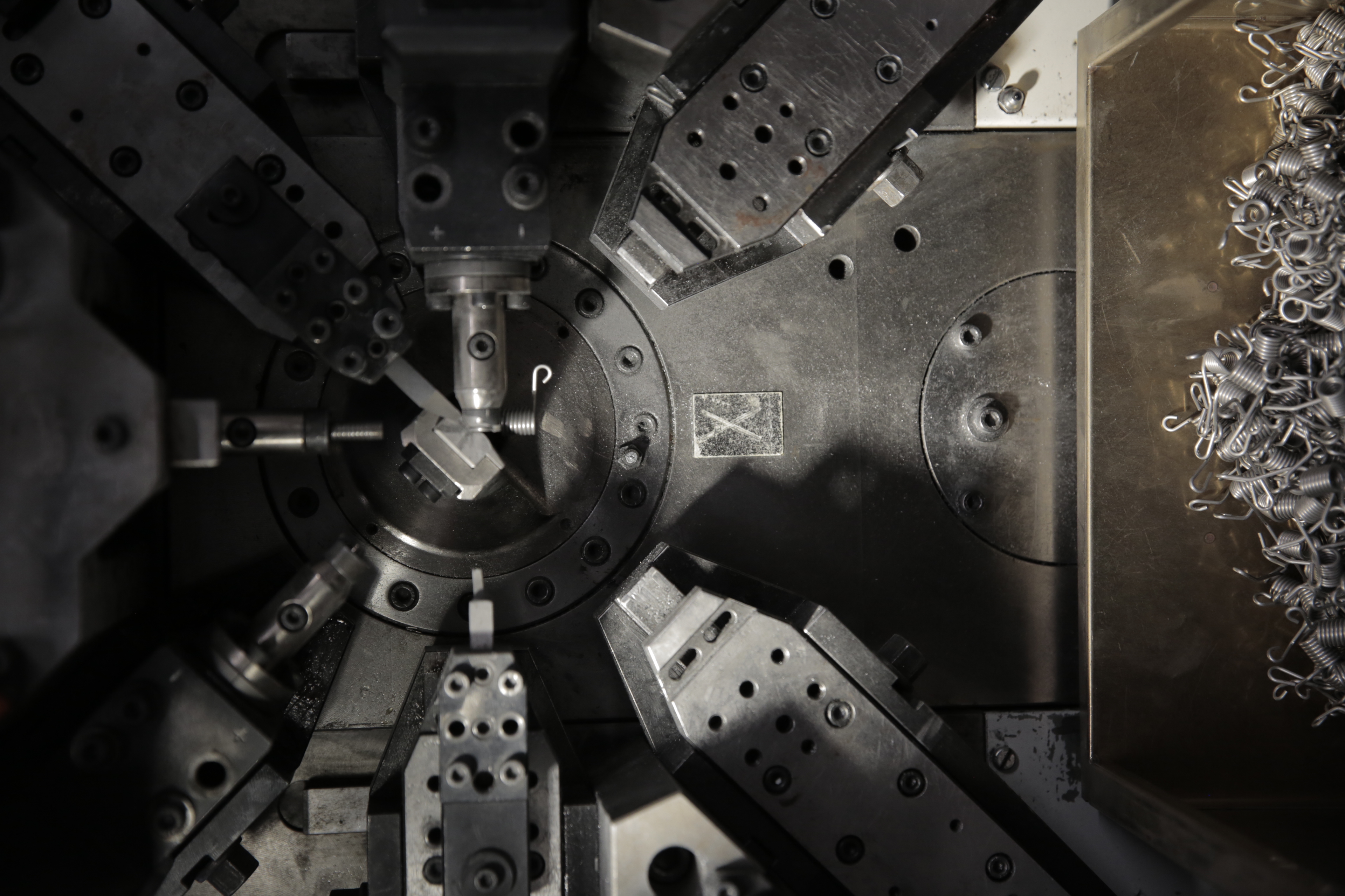 Close-up of an industrial machine's intricate, symmetrical metal components, conveying precision and complexity. Dark tones, with metal shavings below.