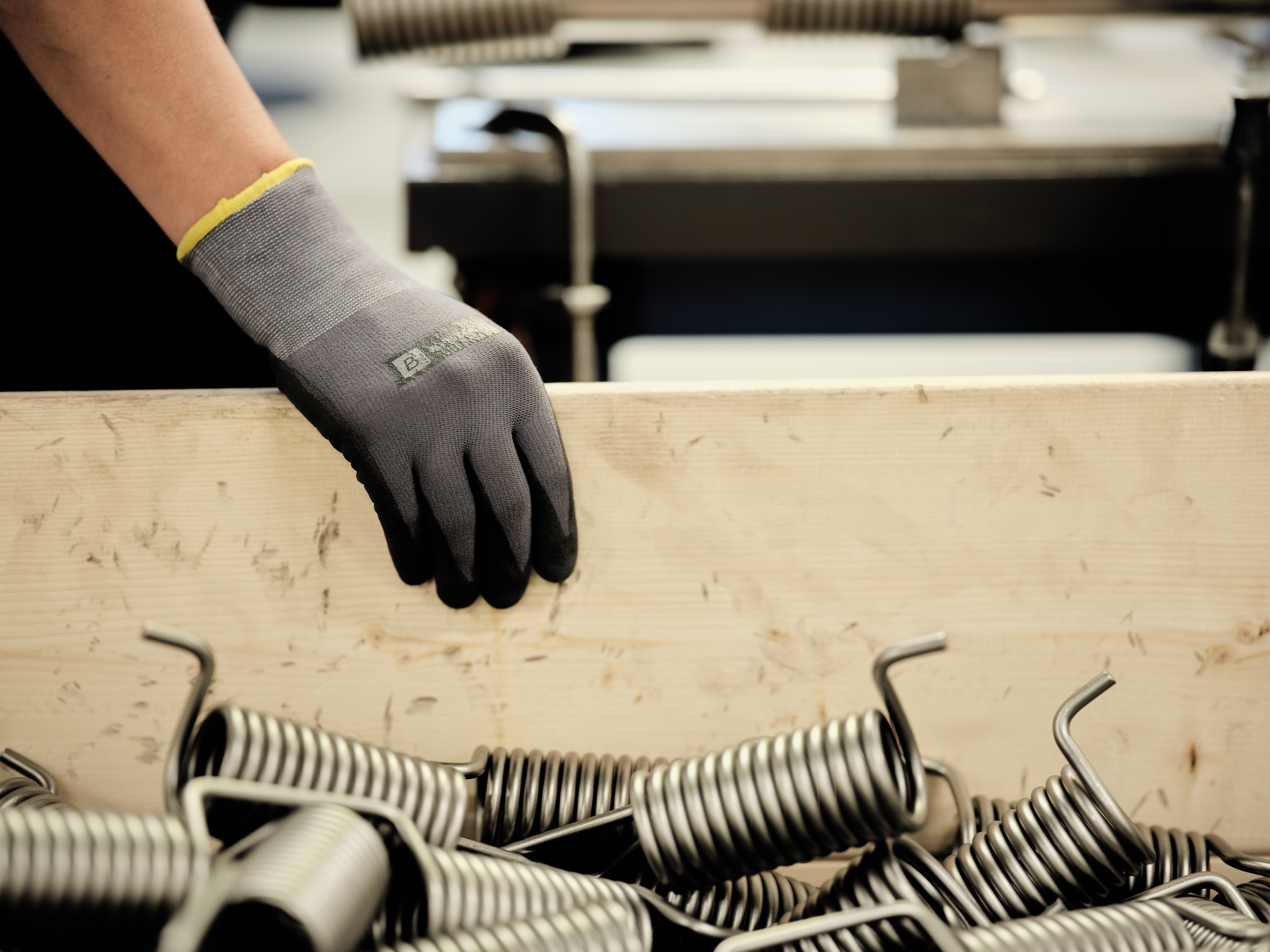 A gloved hand holds a large wooden plank piece behind a box filled with silver metallic torsionsprings.